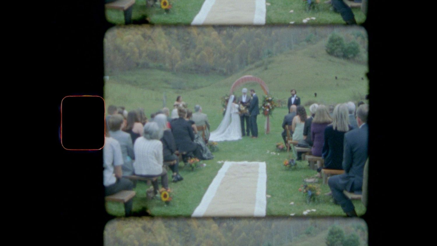 A couple exchanges vows during an outdoor wedding ceremony with guests seated on a grassy hillside.