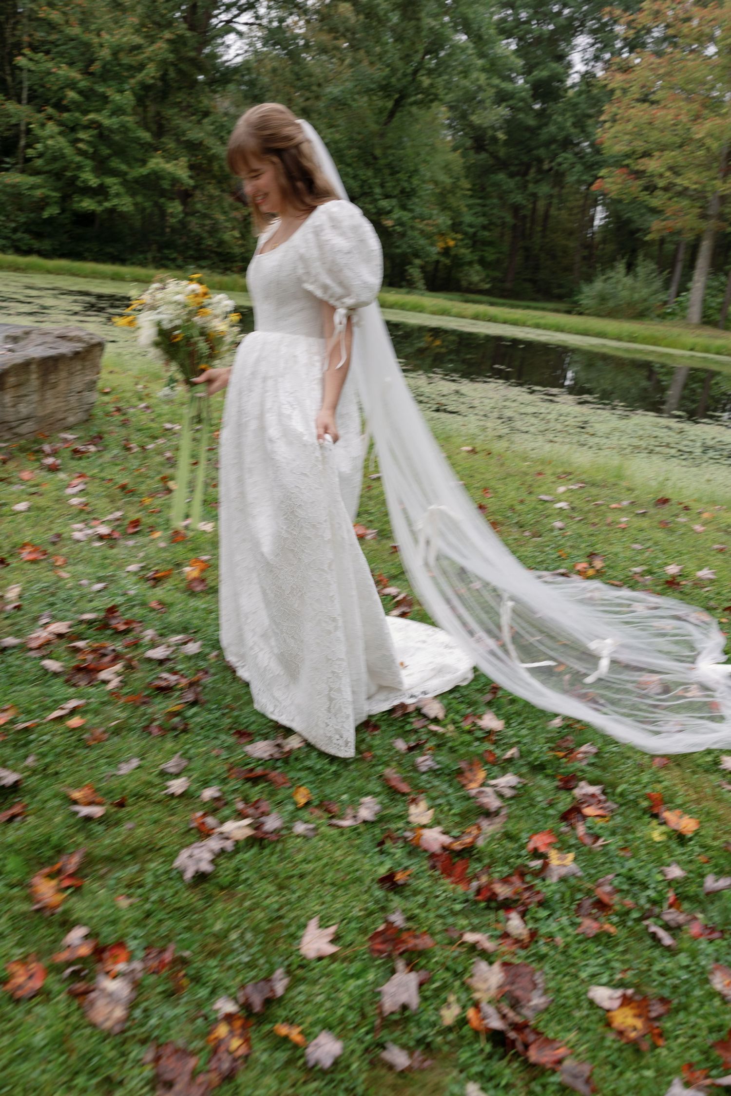 A flowing white dress twirls through an autumn garden with scattered red and orange leaves on the ground.