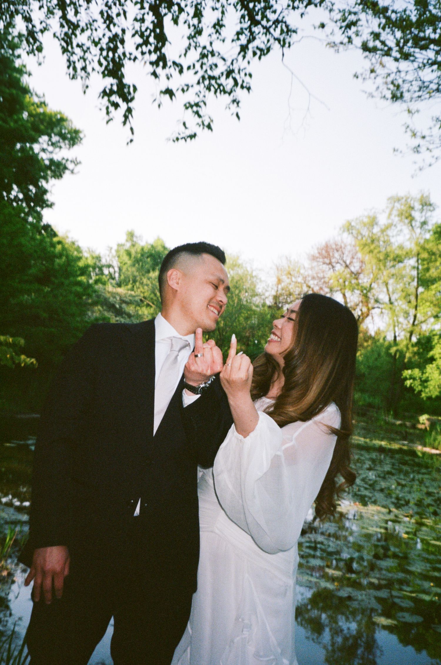 A couple shares an intimate dance together outdoors in a garden setting with lily pads visible in the background.