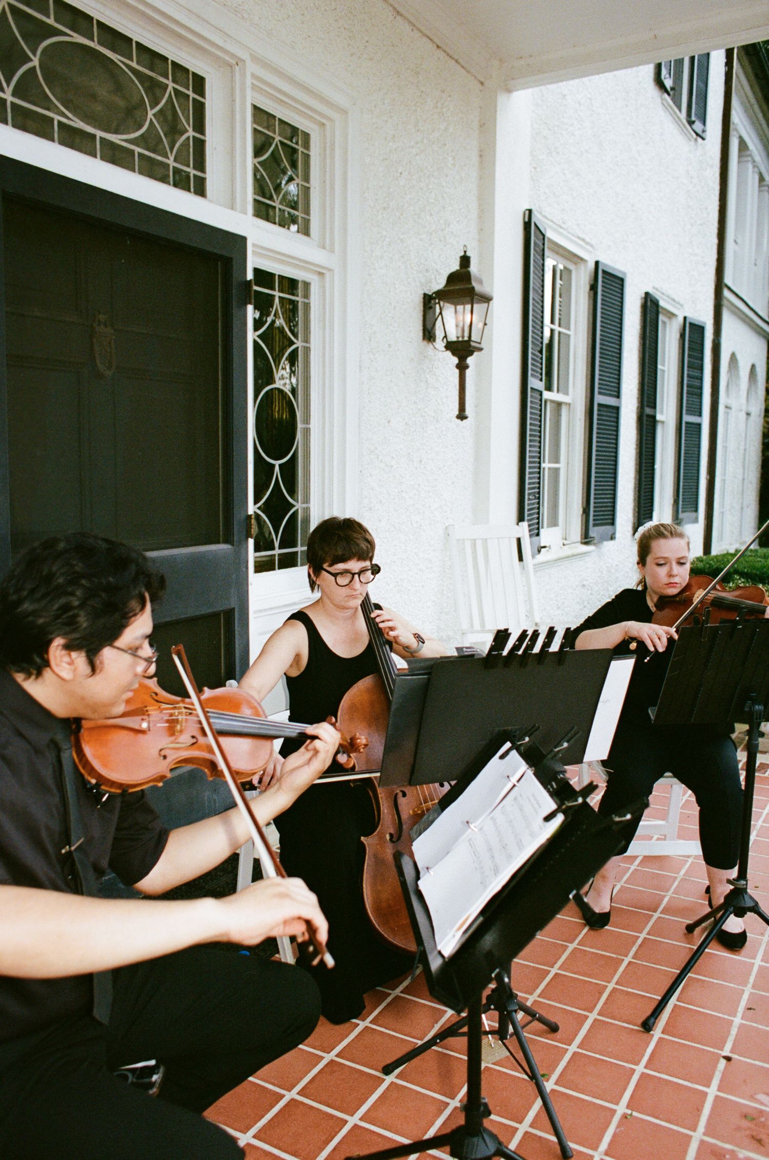 Musicians in black attire perform on string instruments on a terrace with terra cotta tiles.