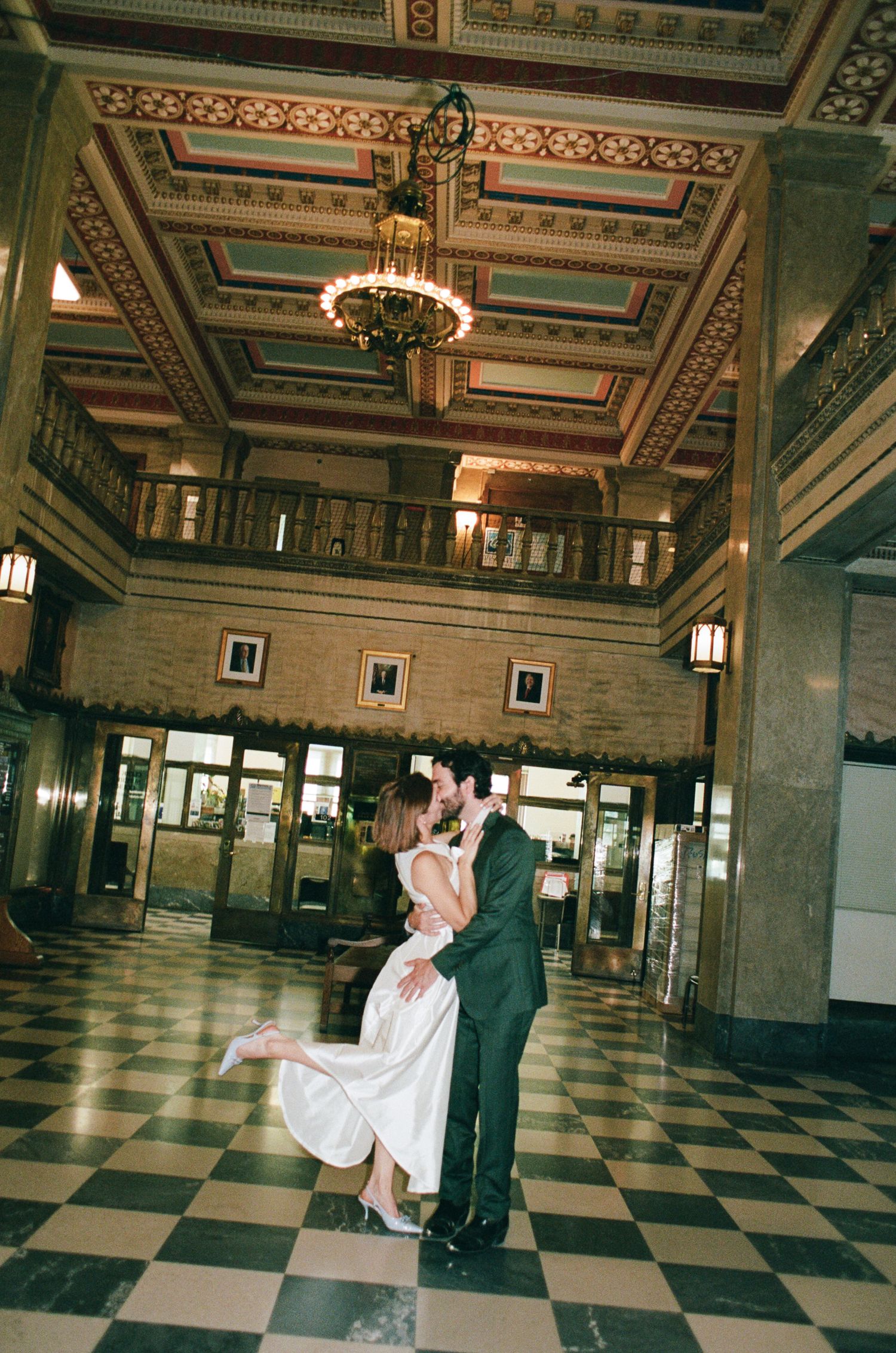 Couple sharing a romantic dance in an elegant hotel lobby with ornate ceiling and chandelier.