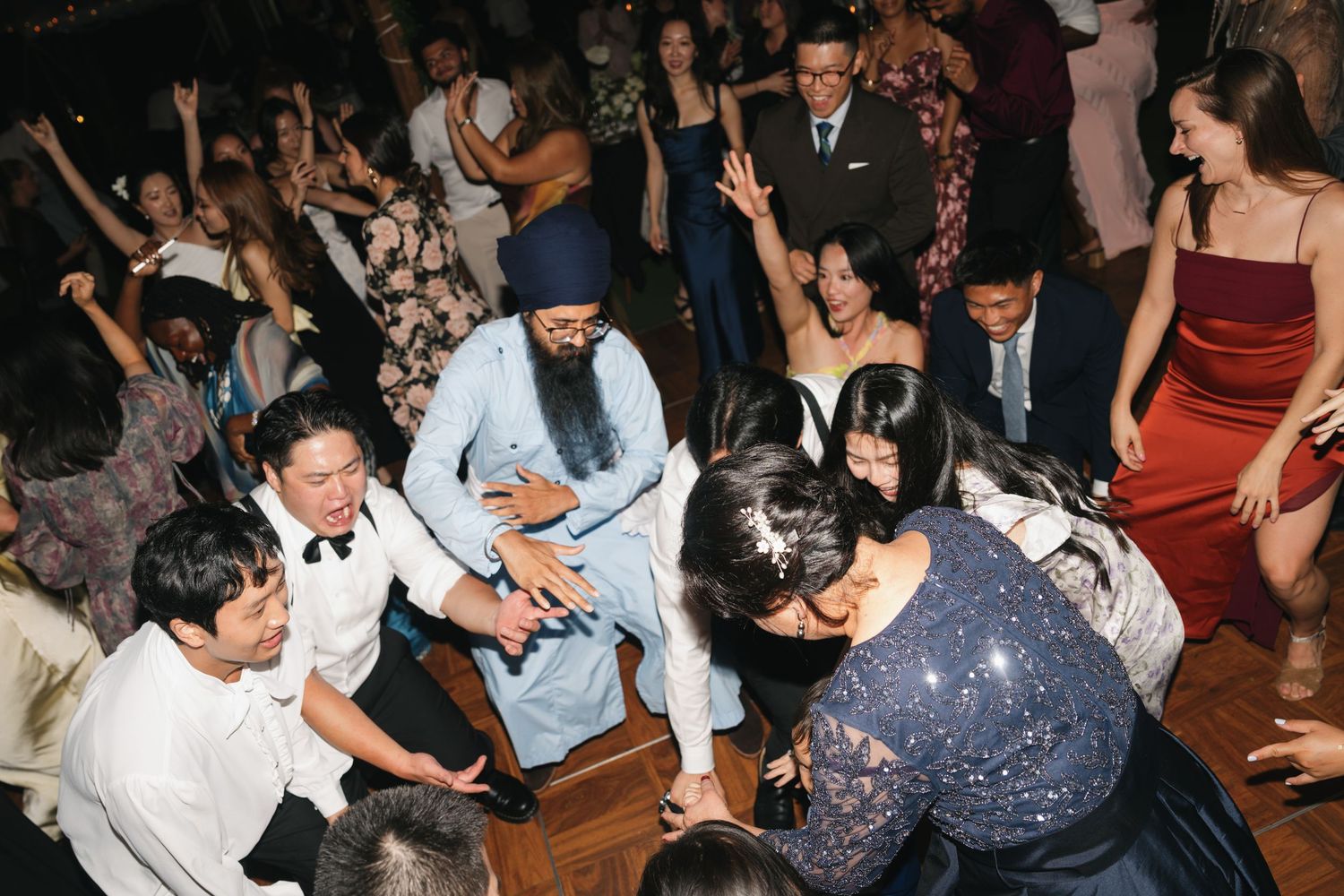A lively crowd of people dancing and celebrating at a wedding reception on a dark dance floor.
