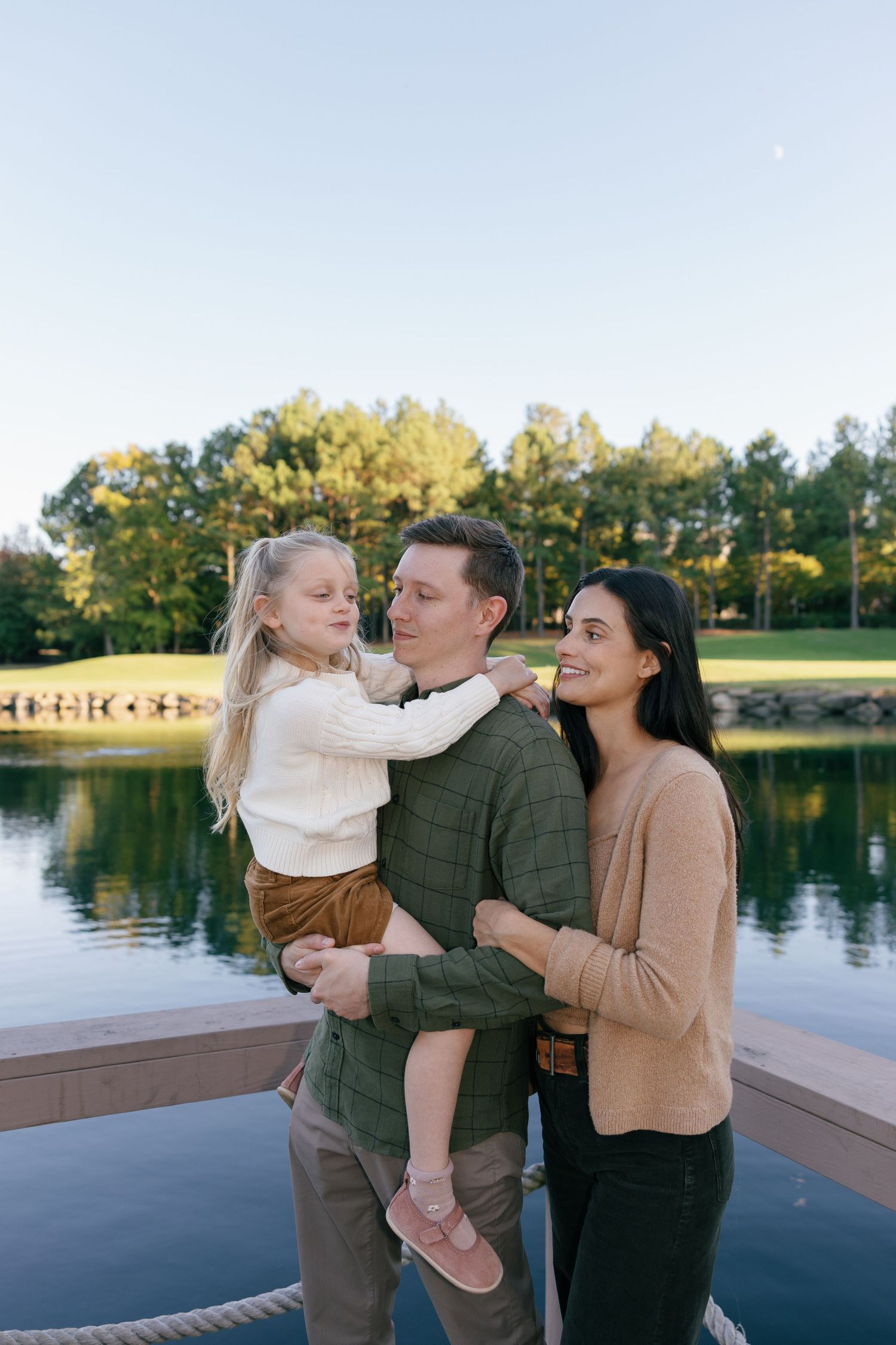 Family shares tender moments together on a lakeside deck during golden hour with water and trees in background.