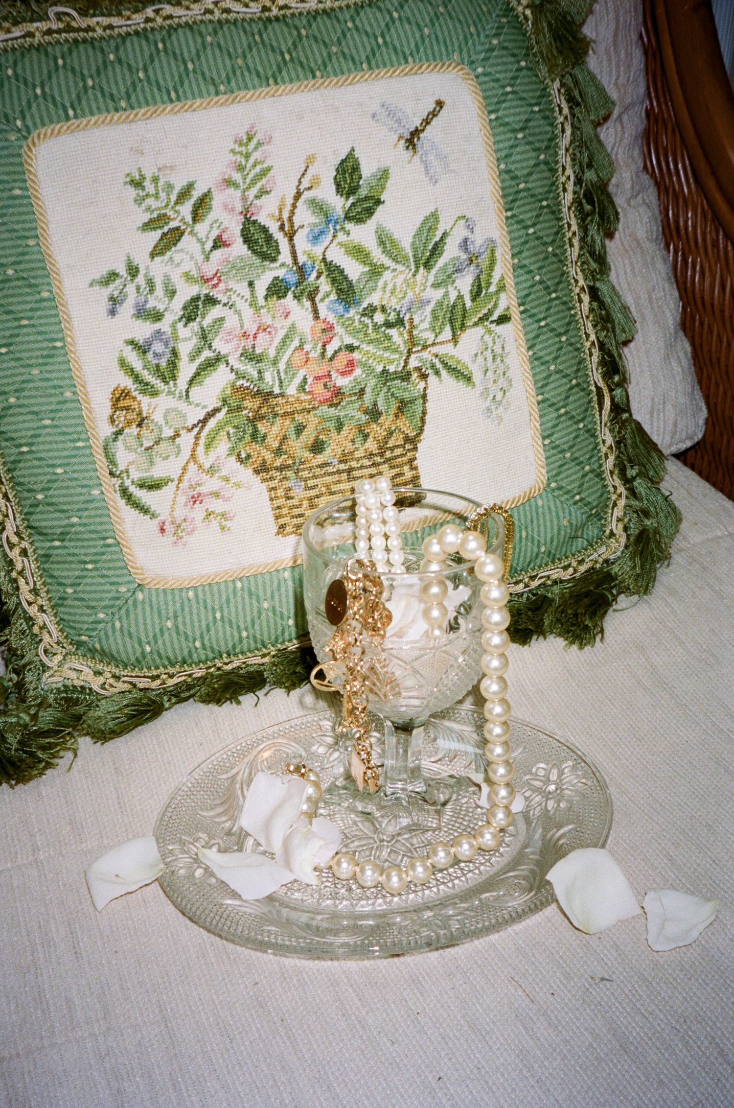 Vintage green pillow with floral embroidery next to pearl necklace and crystal glass.