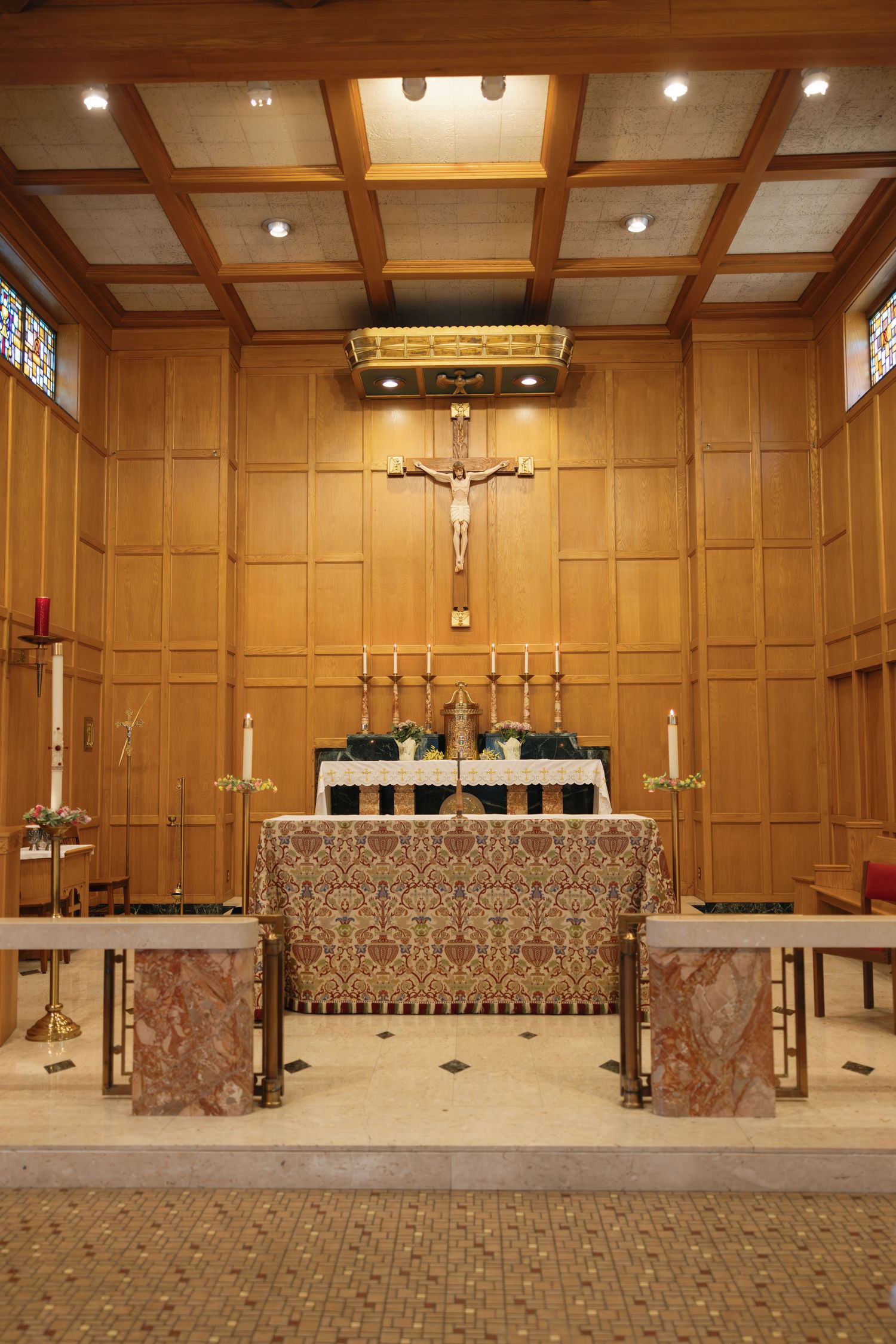 Catholic church altar with crucifix, candles, and ornate altar cloth in a wood-paneled sanctuary.
