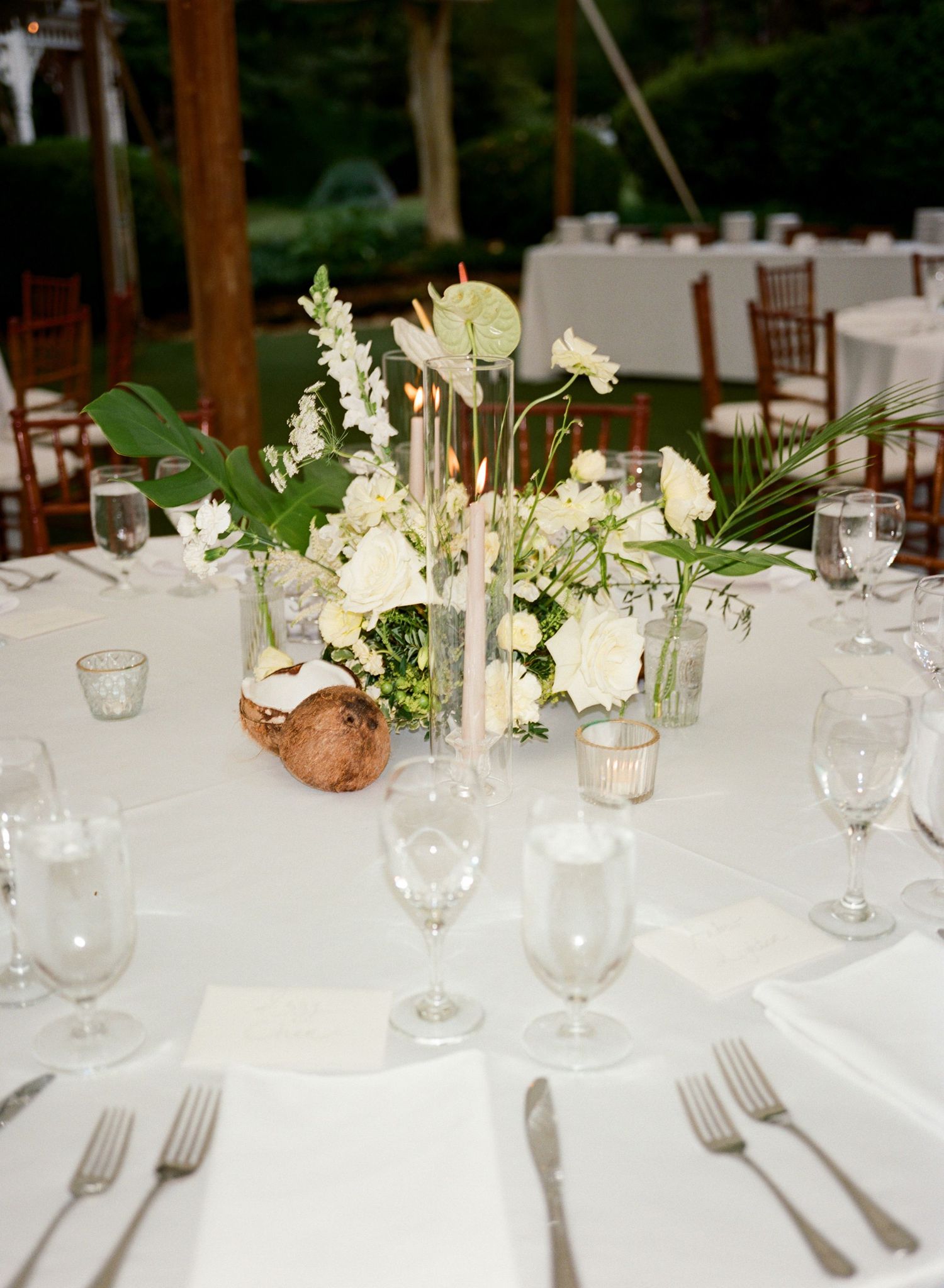 Elegant wedding reception table setting with white linens, glassware, and delicate floral centerpieces in natural light.