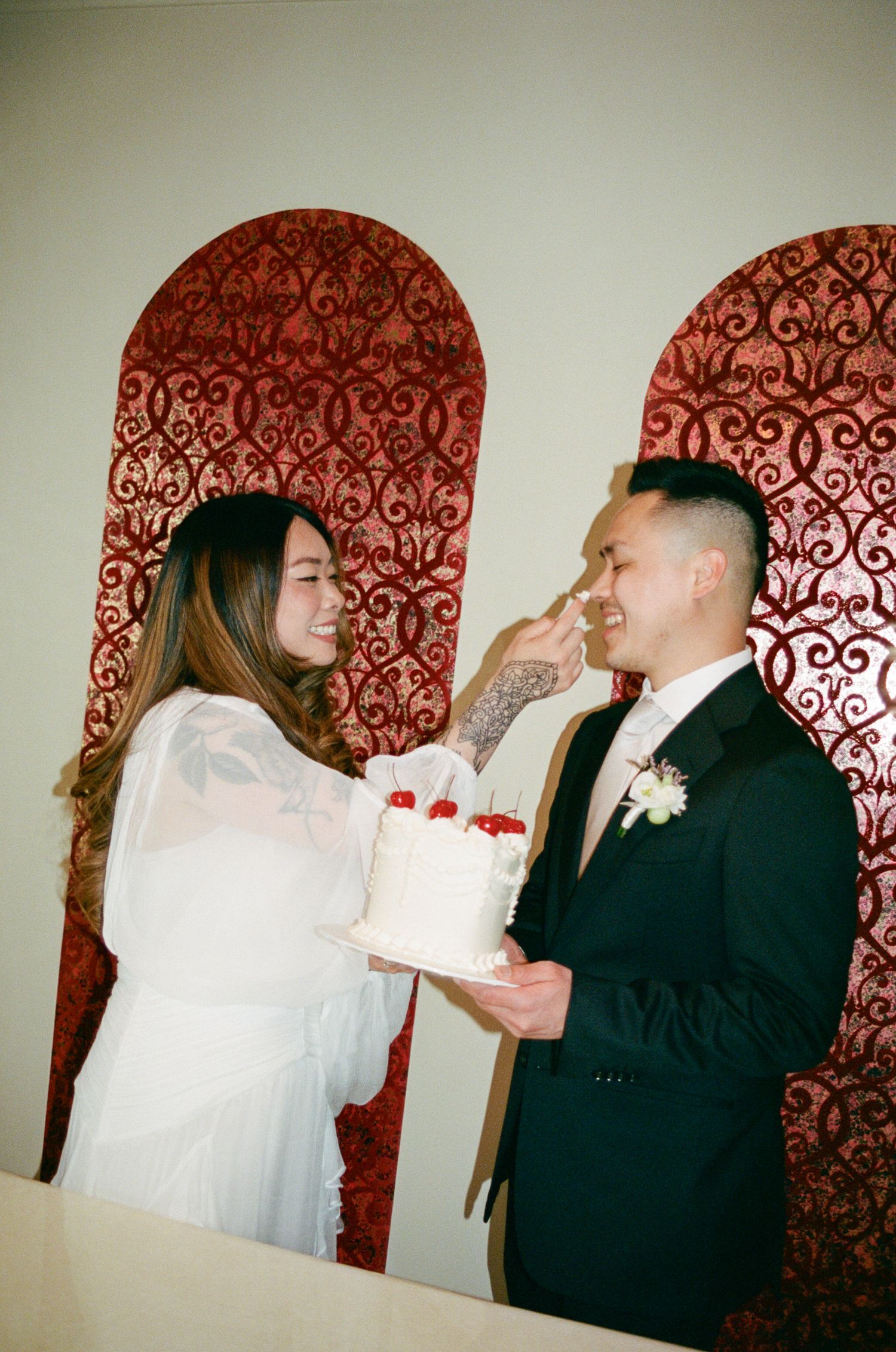 A sequence of photos showing two people in white and black attire playfully feeding each other cake at an event.