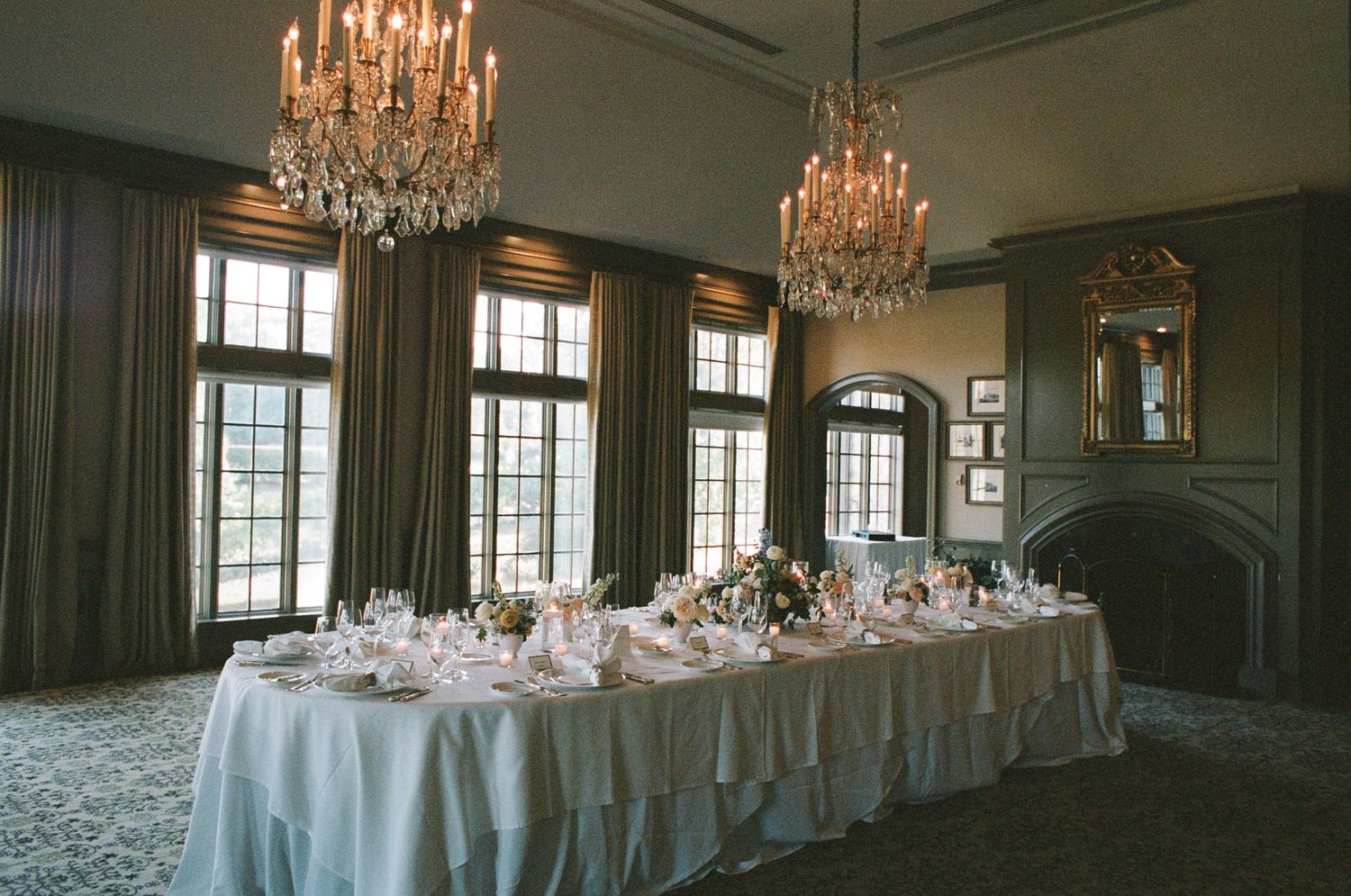Elegant ballroom with crystal chandeliers, tall windows, and white table settings arranged for a formal event.