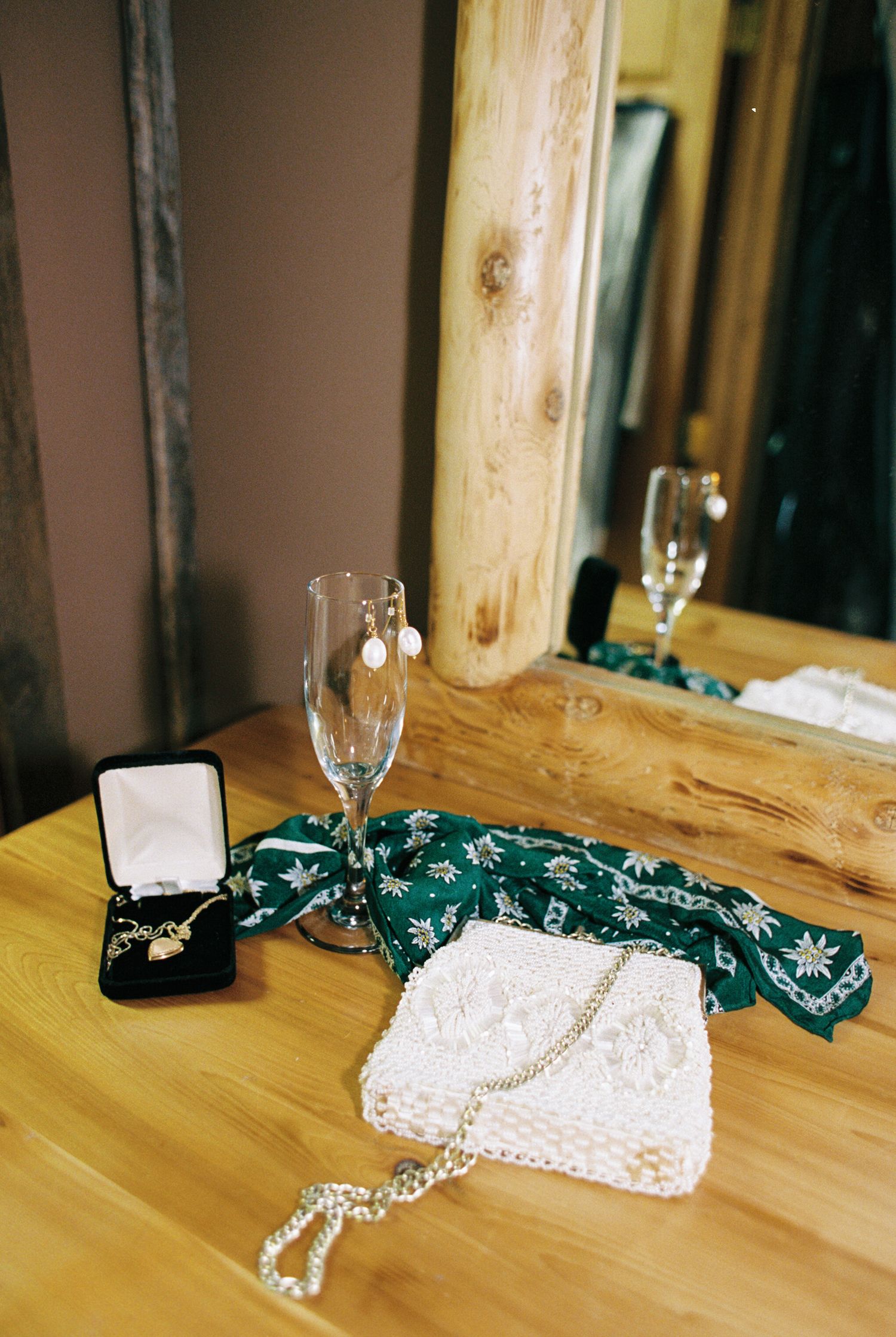 Wedding accessories including a bowtie, champagne flutes, rings, and a white lace clutch arranged on a wooden table.