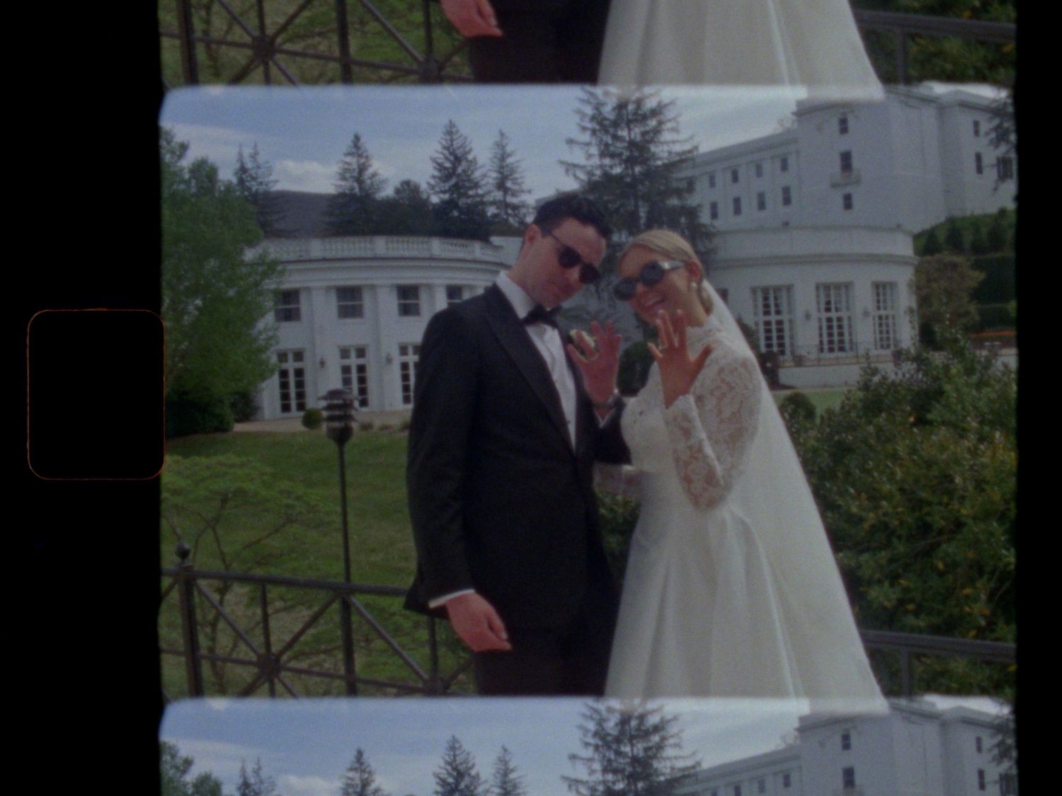 A bride and groom pose together outside a grand white estate on their wedding day.