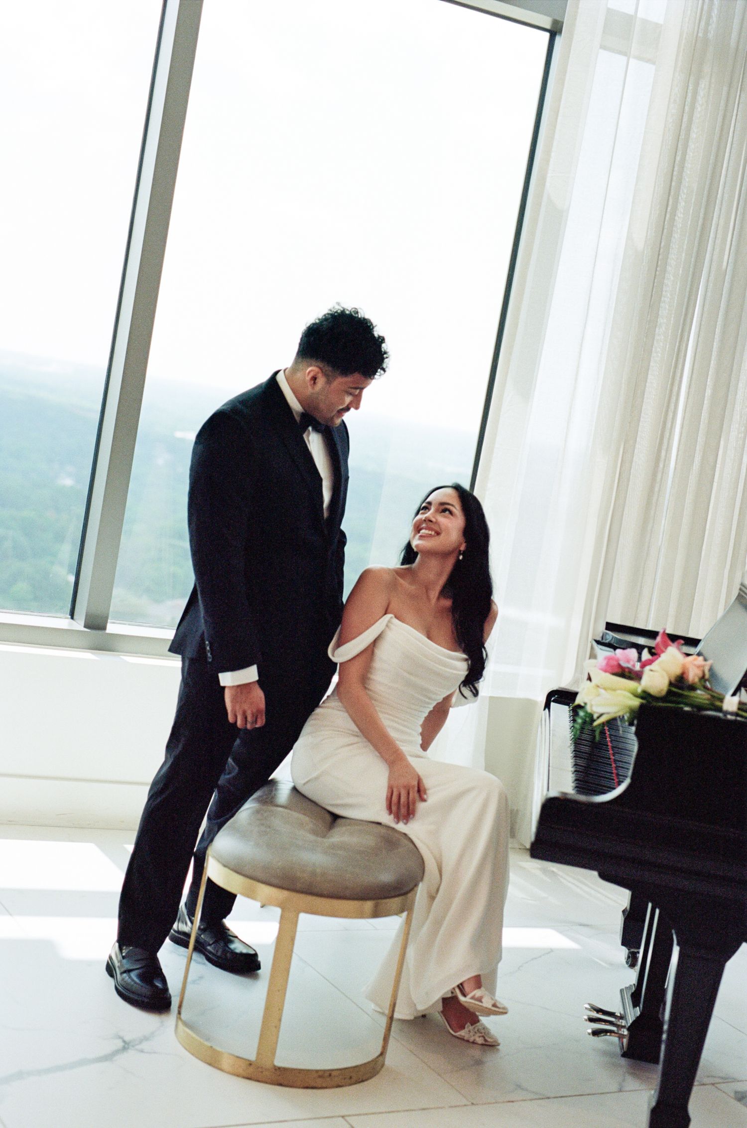 A couple shares a playful moment together in a bright modern room with floor-to-ceiling windows and scenic views.