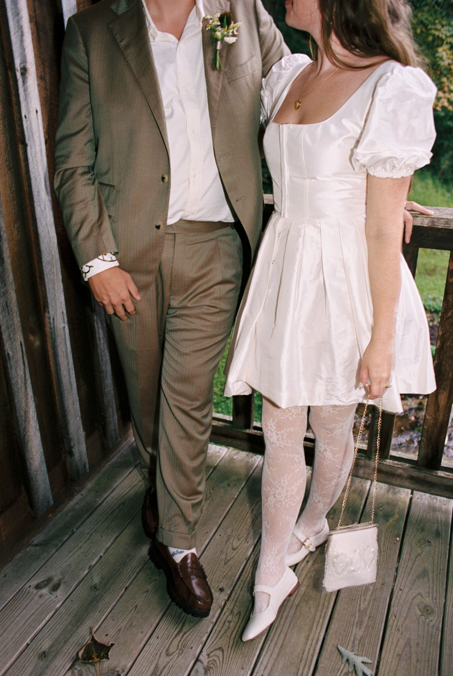 Legs of people in white and brown formal attire standing on a wooden deck or boardwalk.