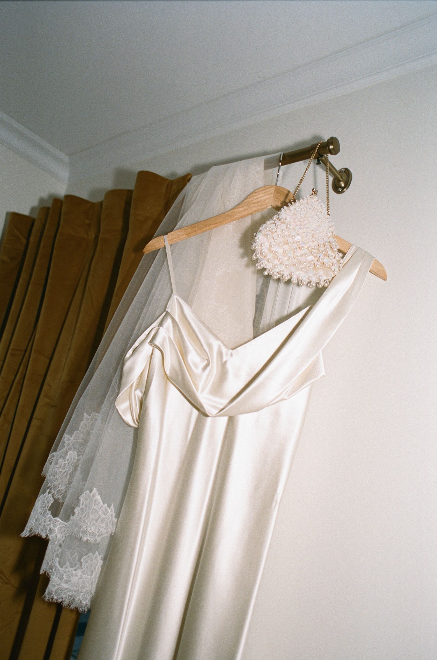 White wedding dress hanging on wooden hanger with pearl accessory.
