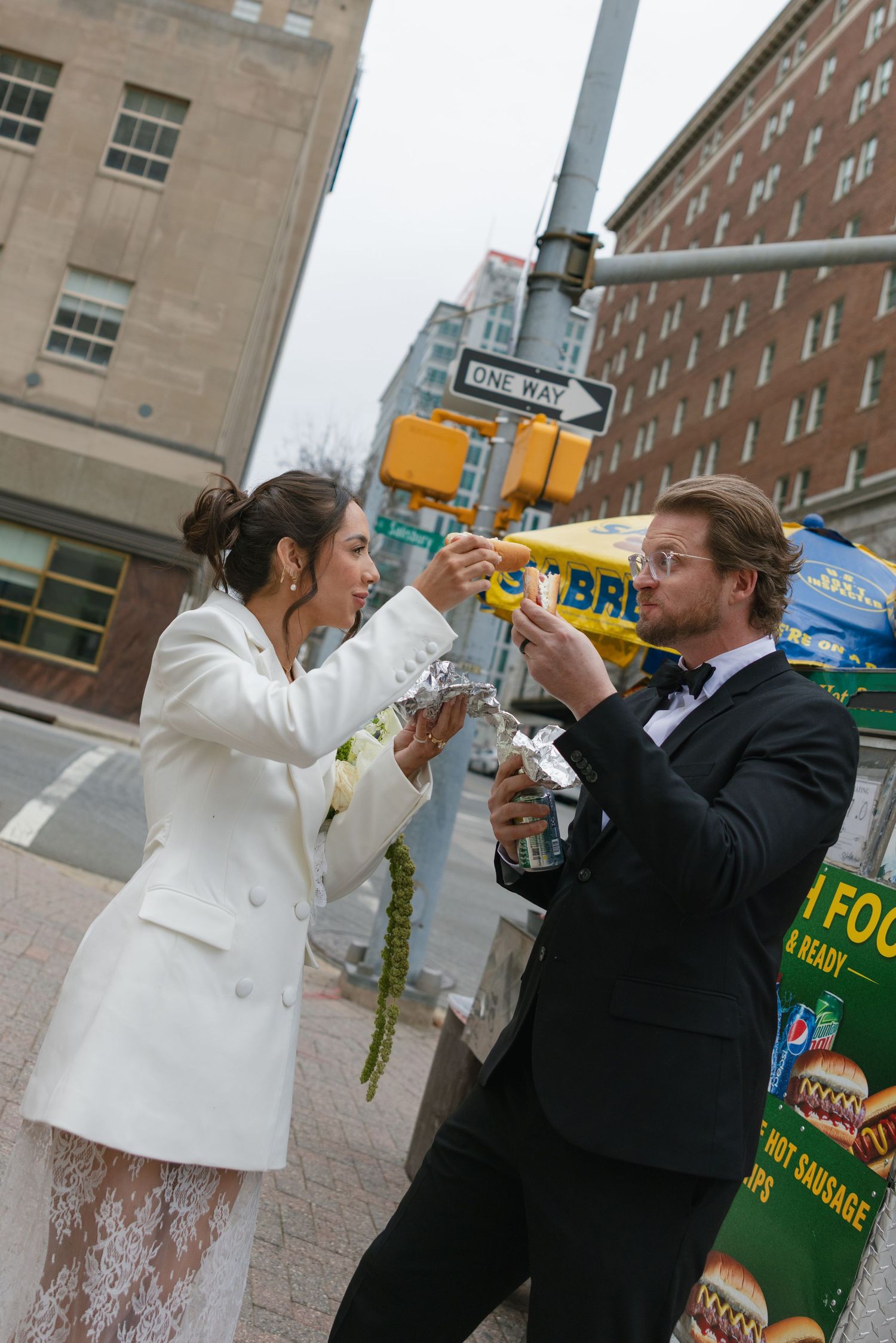 Bride and groom toasting with drinks at a NYC street corner near a One Way sign on their wedding day.