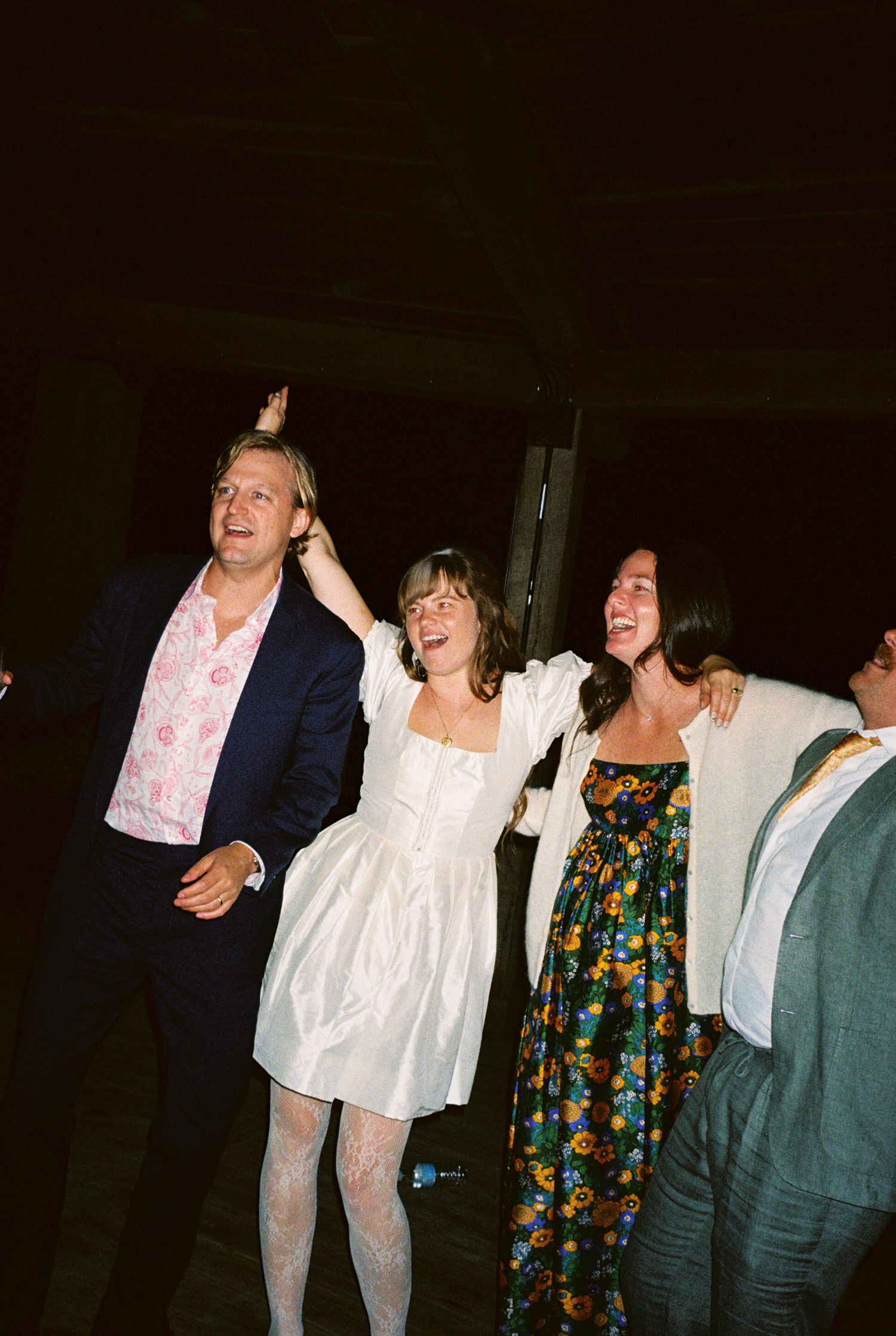 A group of people laughing and dancing together at a dimly lit indoor gathering.