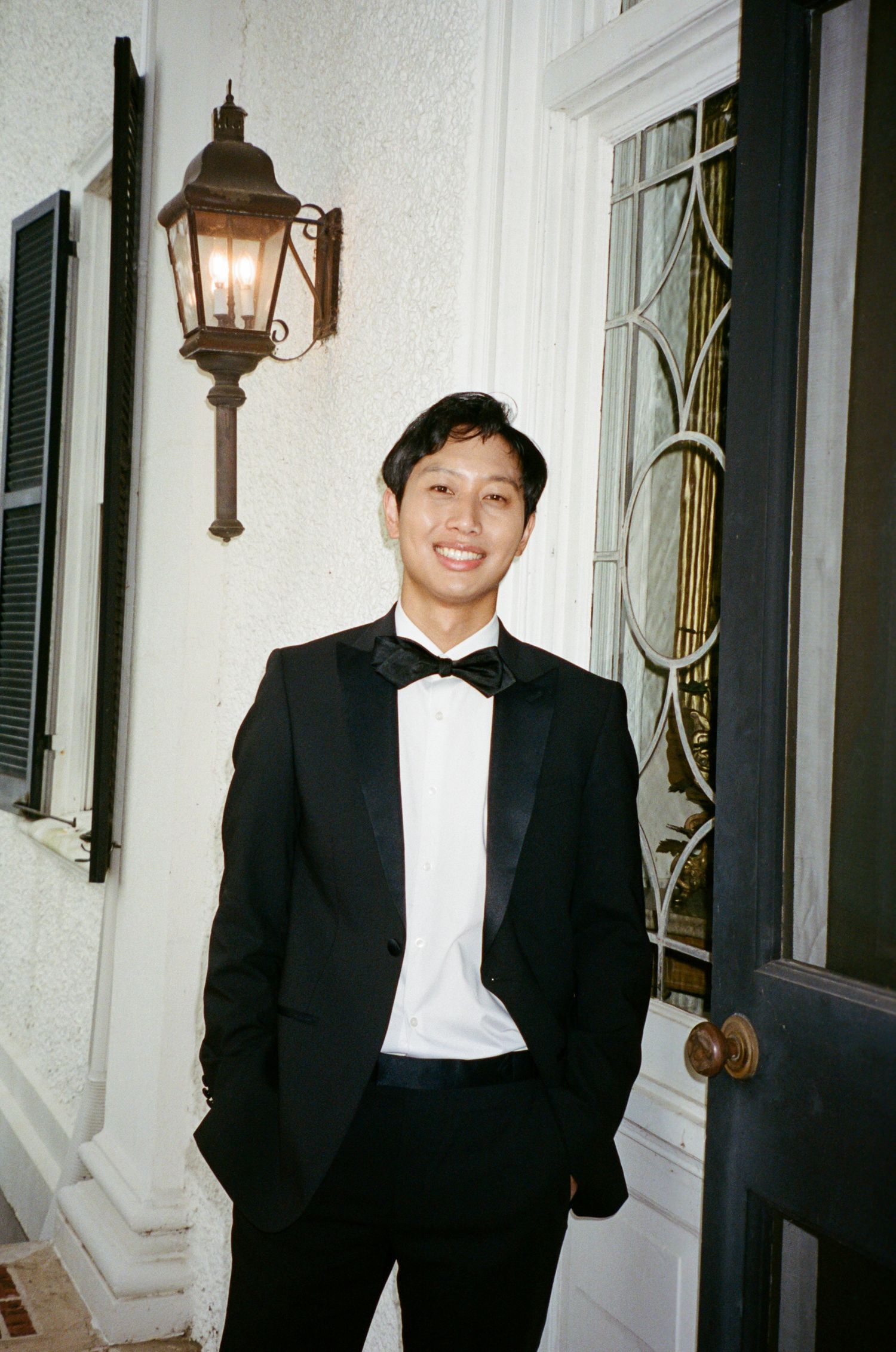 Three elegant black and white tuxedo portraits showing someone posing against a white wall with vintage wall lamps.