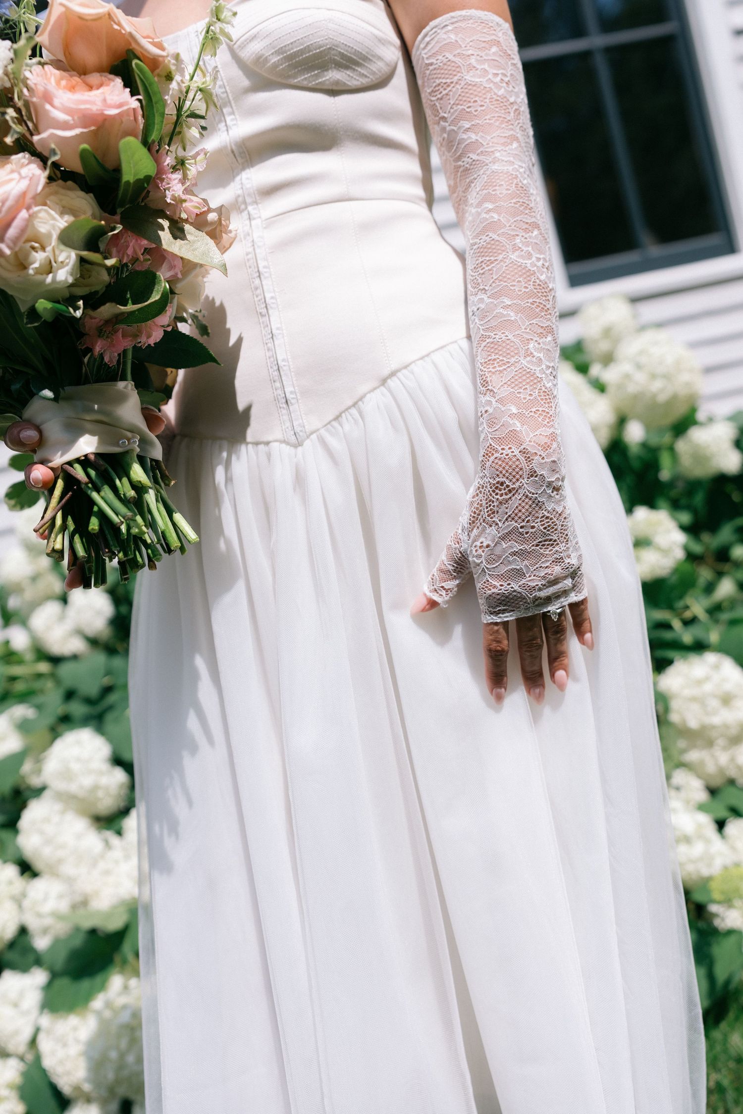 Close up details of delicate white lace sleeves on an elegant bridal gown with white hydrangeas in the background.