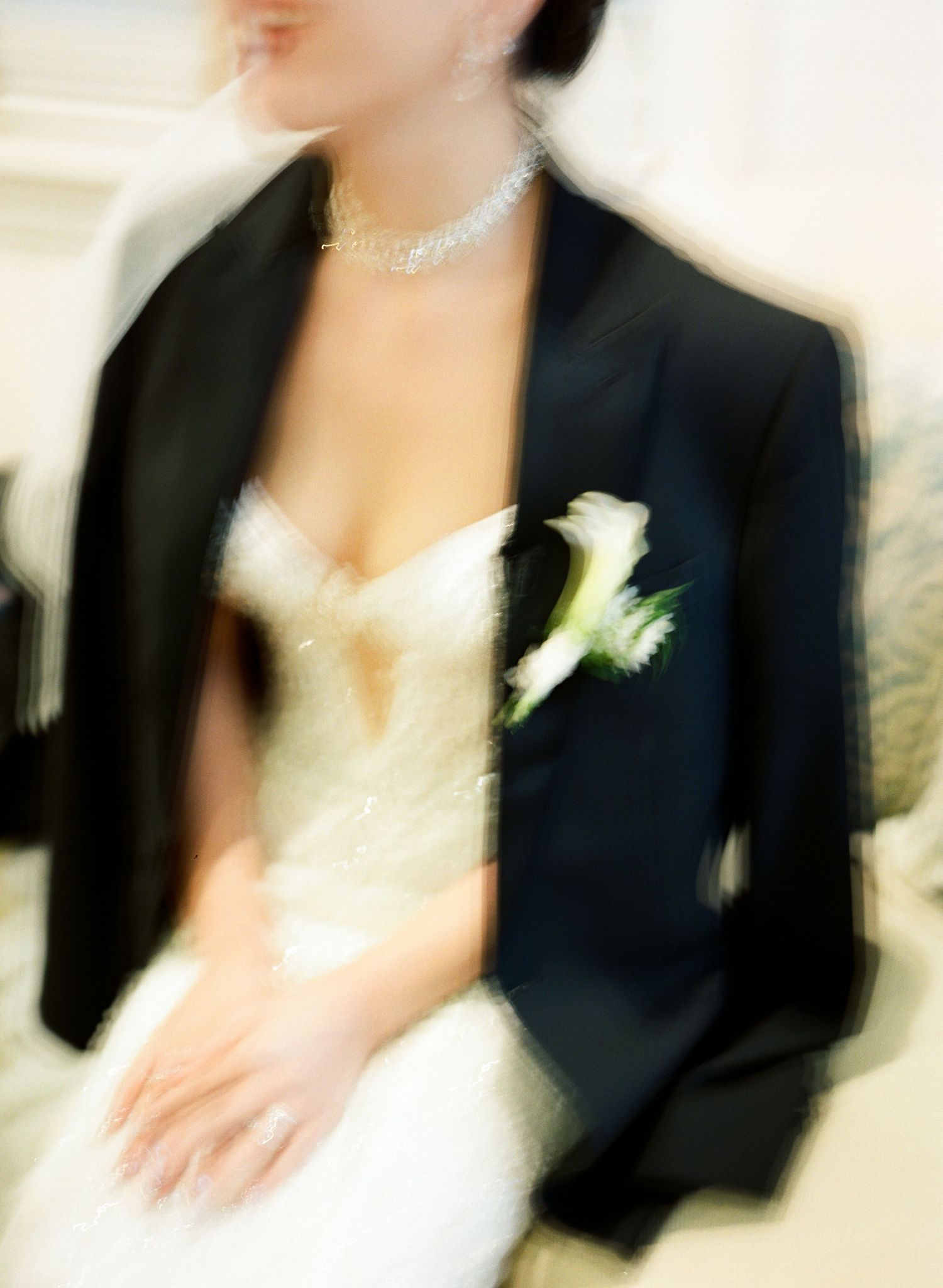 A person in formal black attire with a white boutonniere in a soft focus wedding photography style.