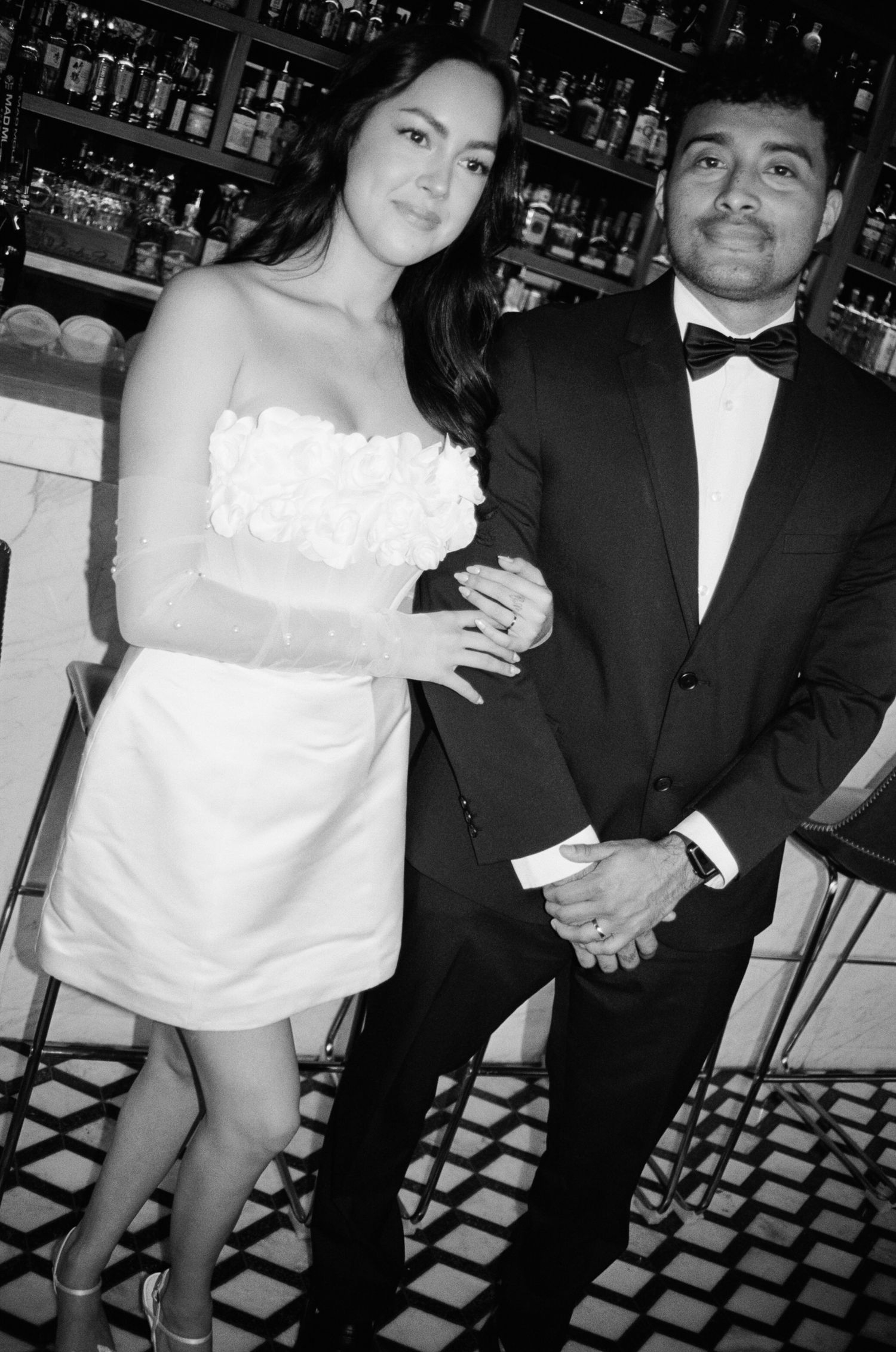 Black and white photo series showing a couple at a bar in formal attire with a white off-shoulder dress and dark suit.