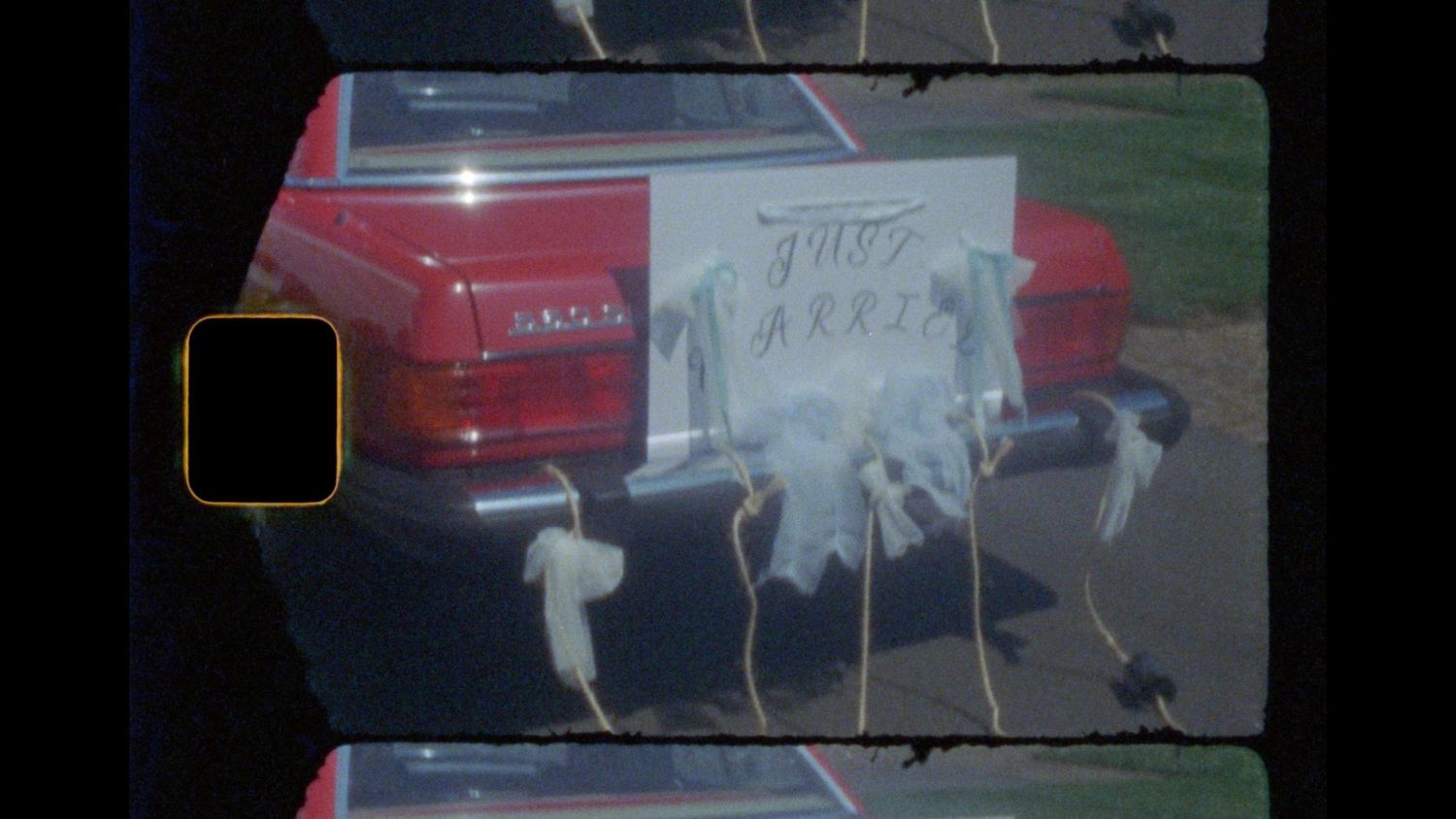 Red vintage convertible with a just married sign and ribbons tied to the rear bumper, shown in a retro film strip frame.