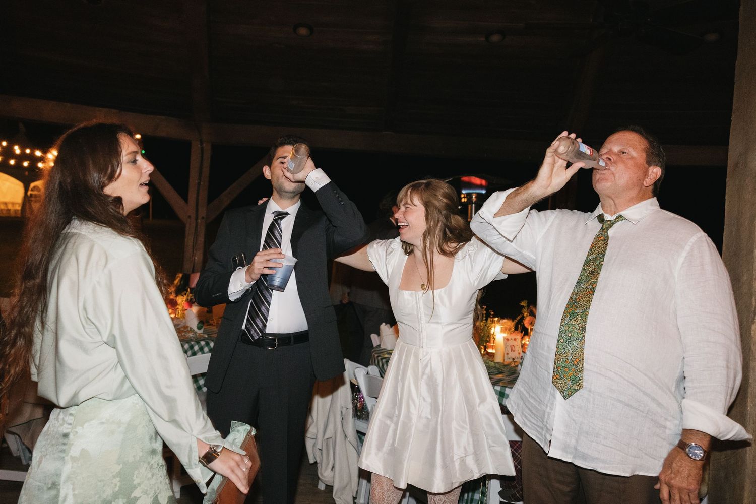 People dancing and celebrating at a wedding reception in a dimly lit venue with festive decorations.
