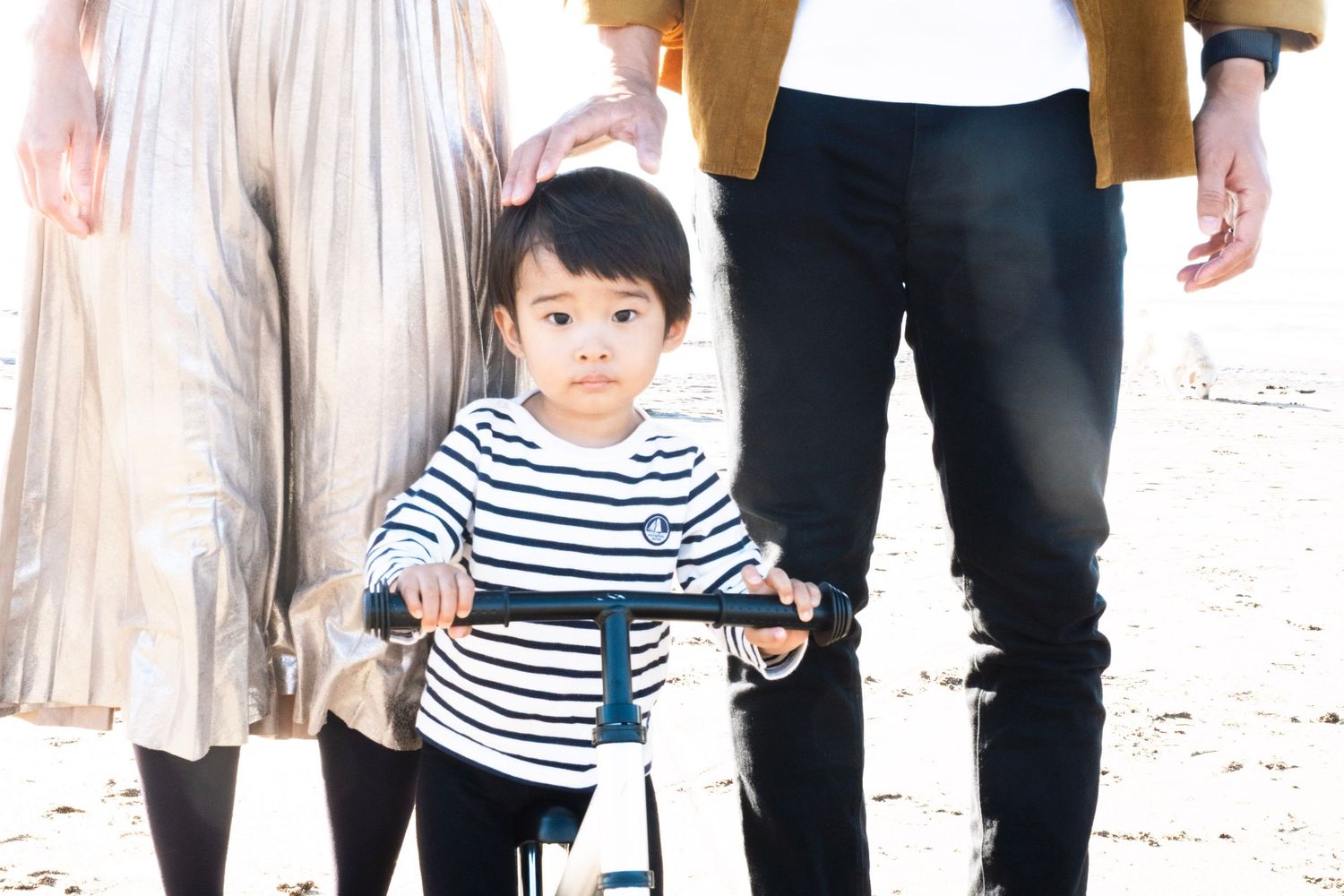 A child wearing a striped shirt walks between adults on a bright white background. browns bay auckland. daydreampics