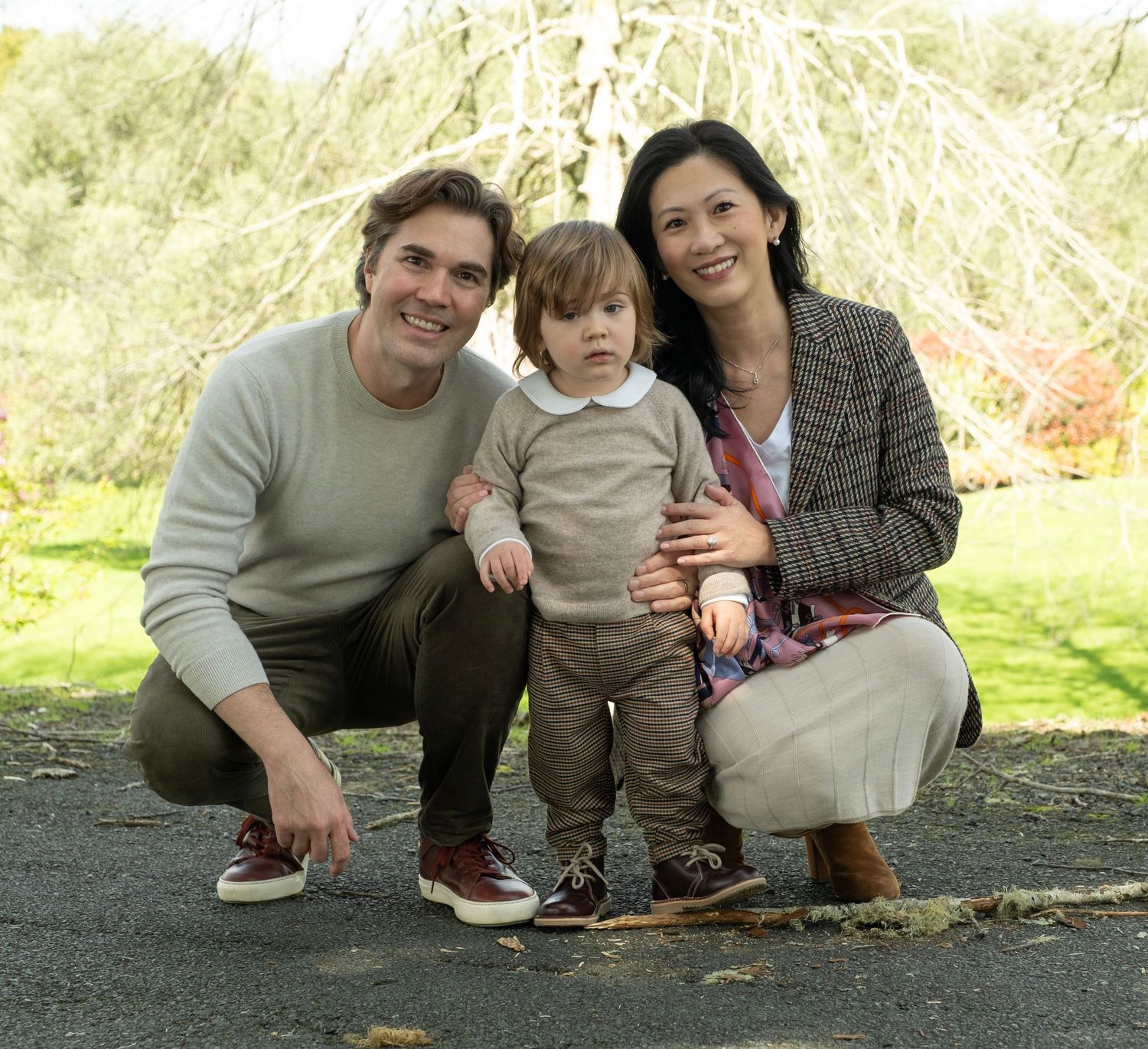 A family of three poses together outdoors on a sunny day with green grass and trees in the background. auckland daydreampics