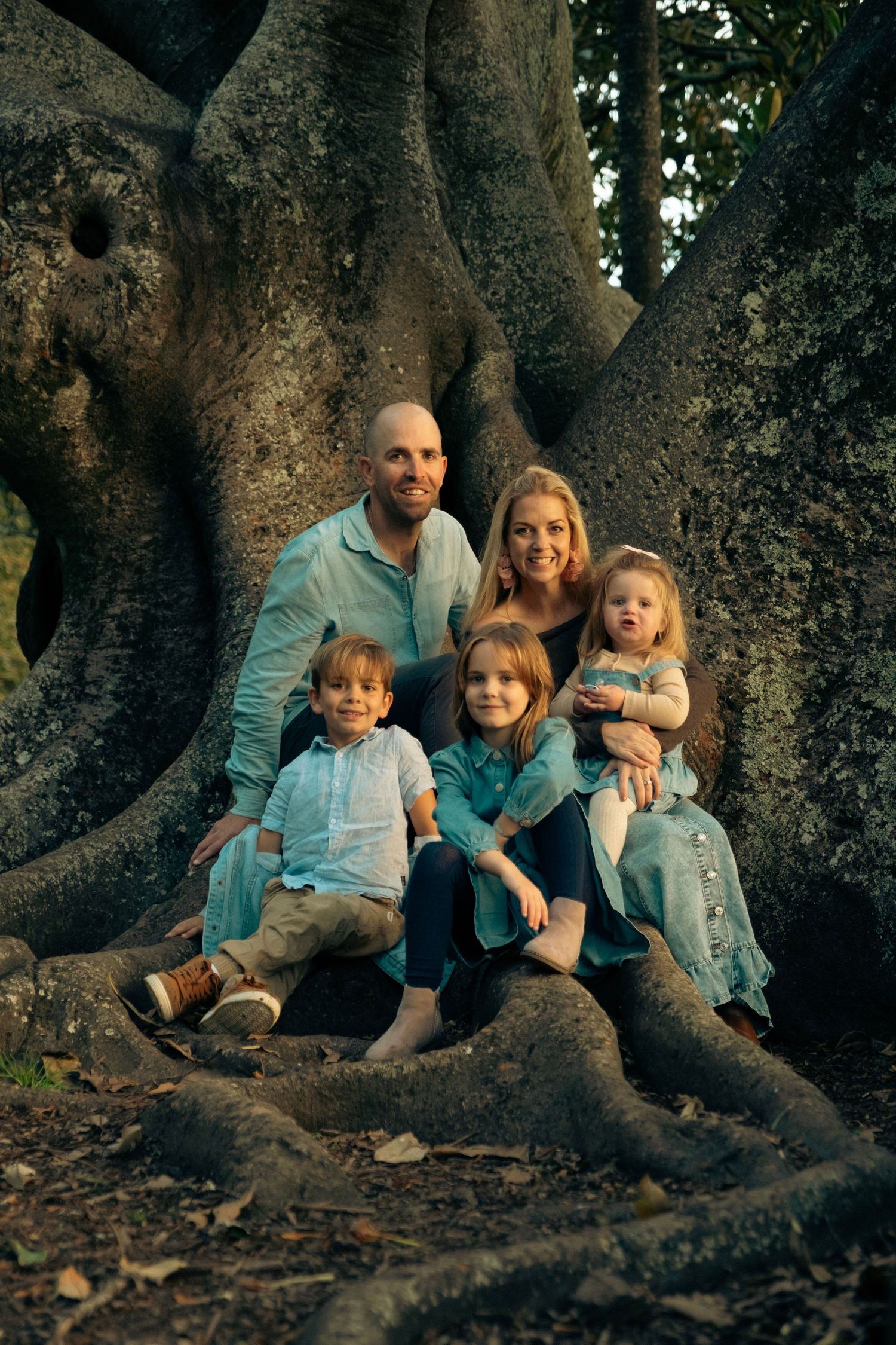 A family sits together on large tree roots in a natural outdoor setting at dusk. sunset autumn cornwall park. auckland. daydreampics