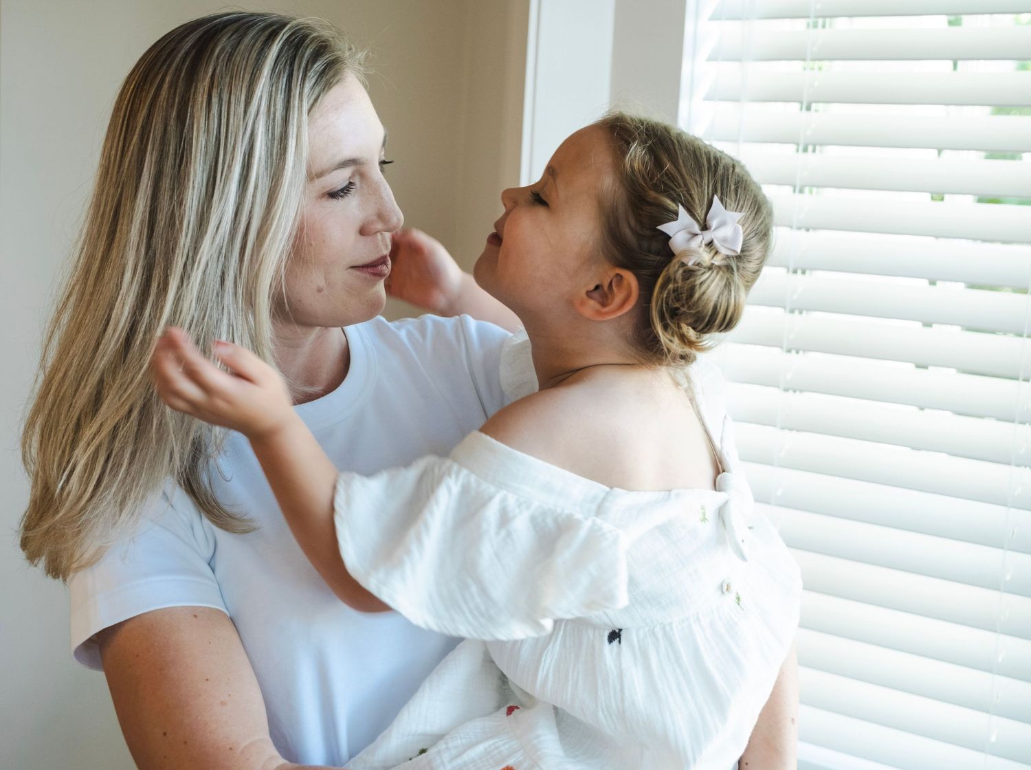 A tender loving moment between parent and child in white clothing near a window with venetian blinds. auckland mount eden