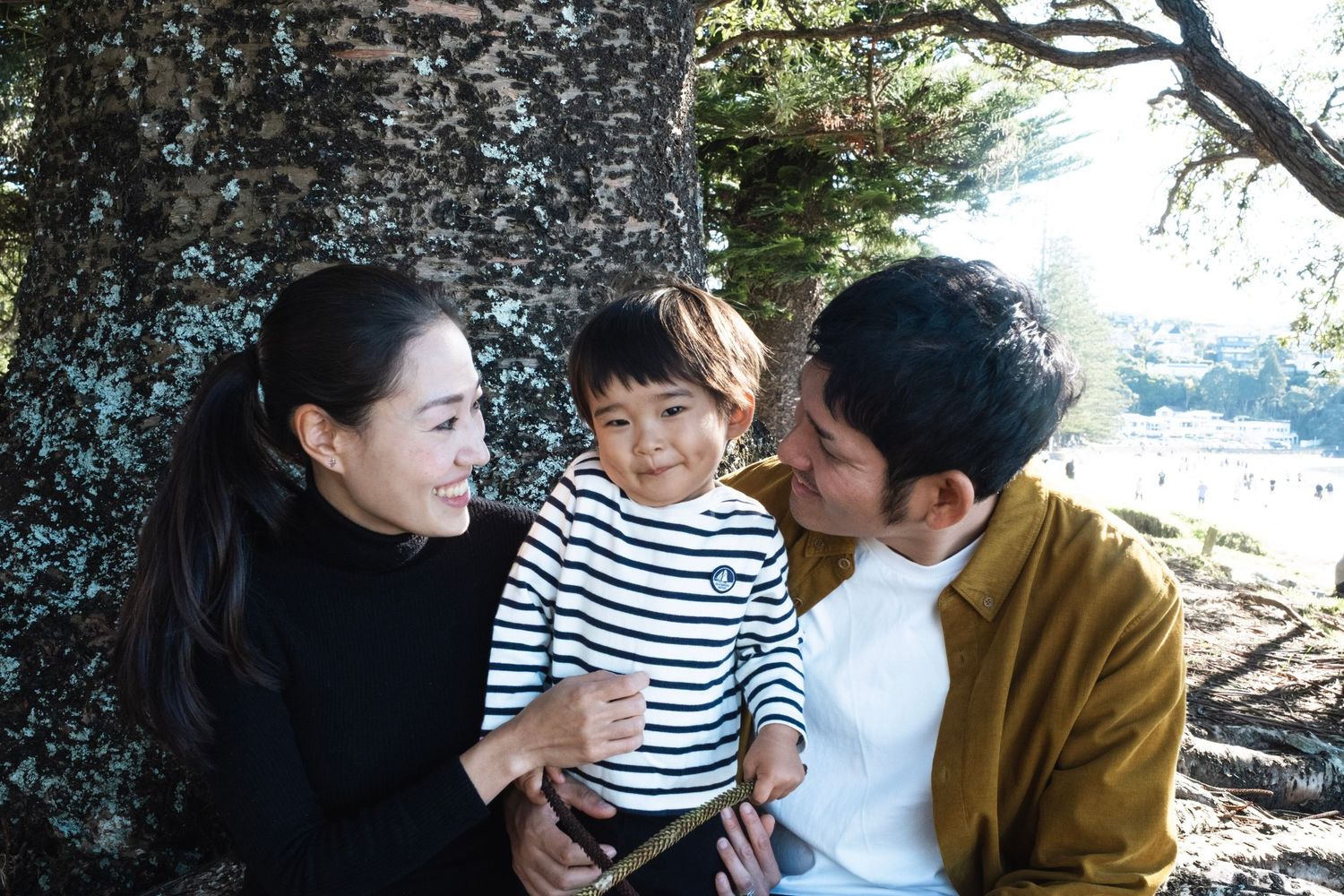 Three people interact playfully while sitting together outdoors among trees and natural scenery. browns bay