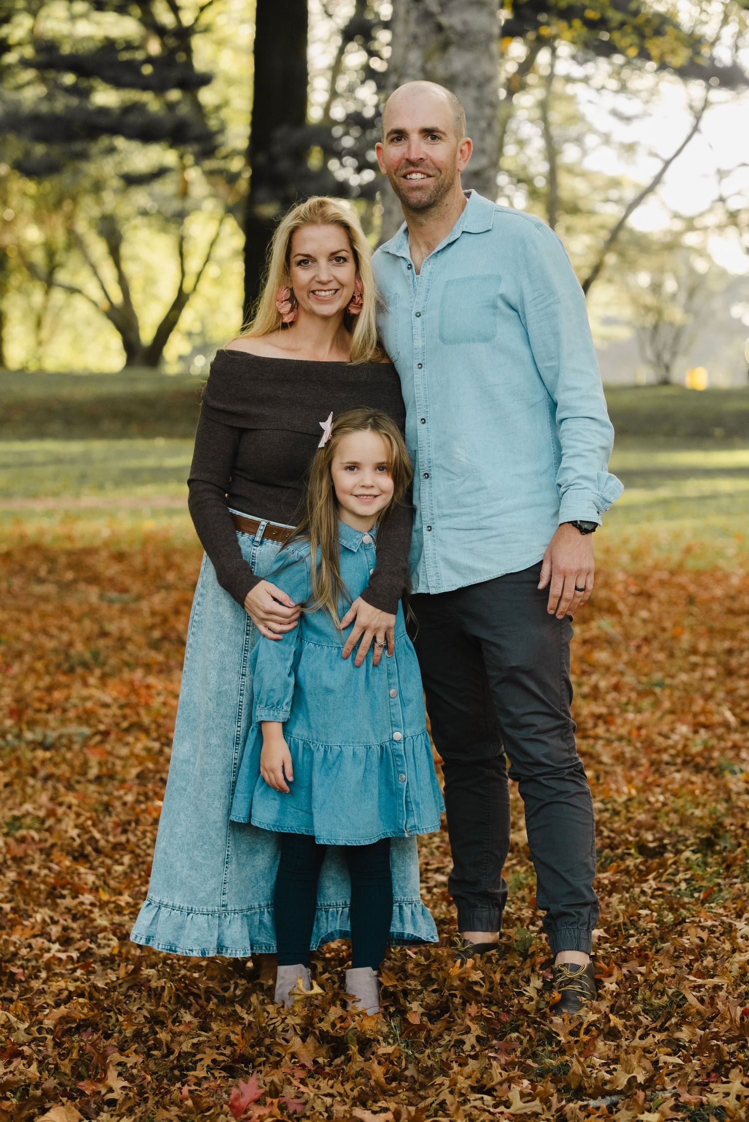 Family wearing coordinating turquoise and black outfits poses together on autumn leaves in park setting. cornwall park daydreampics