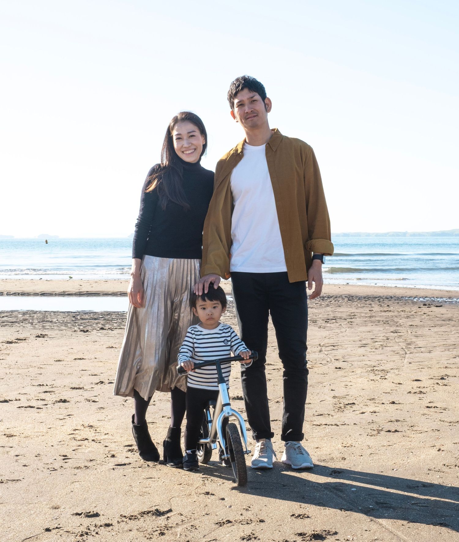 A family poses together on the beach with a child on a bicycle while enjoying a sunny day by the ocean. daydreampics