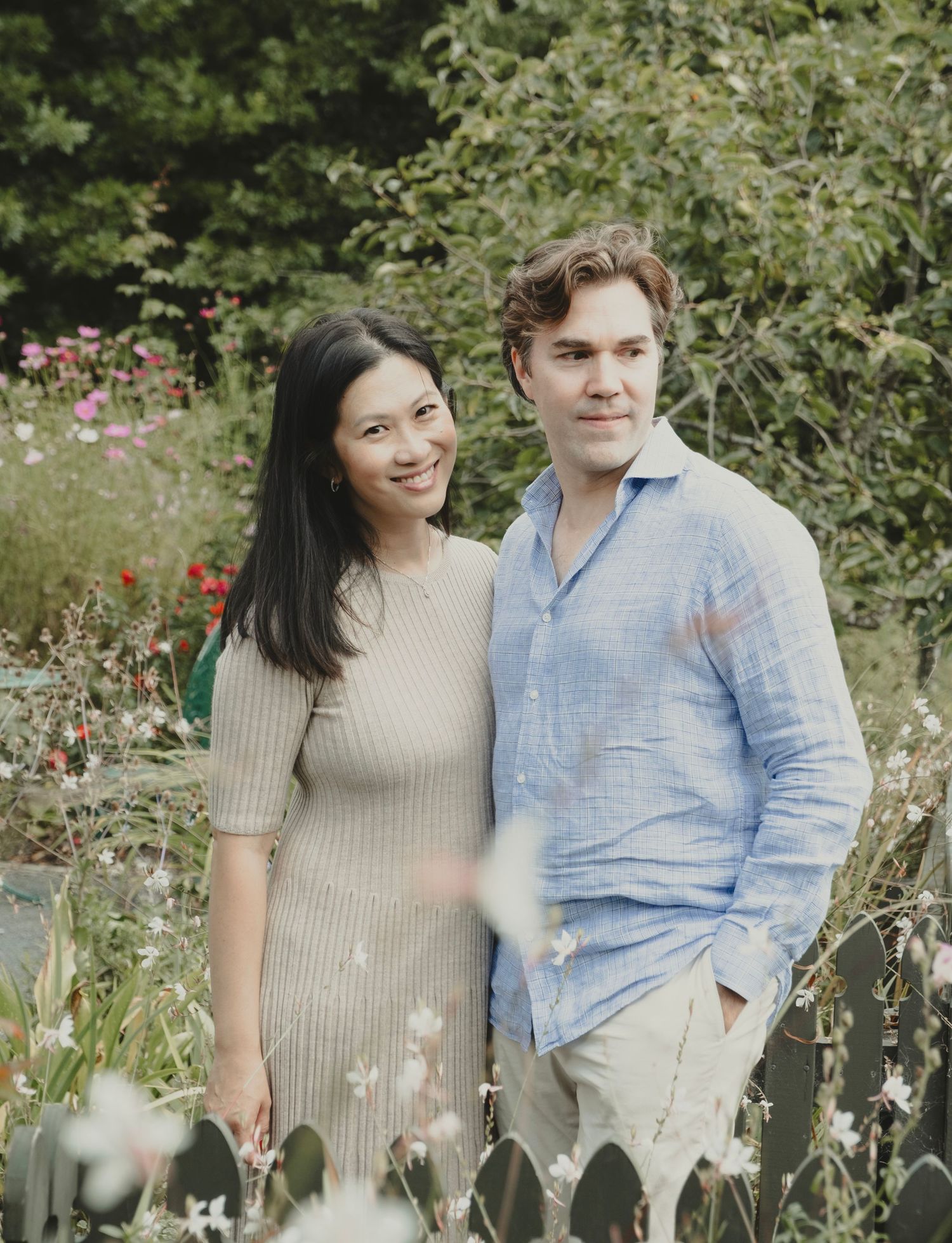 A couple sits together on a garden bench surrounded by blooming flowers and greenery in a romantic outdoor setting. mincher gardens auckland