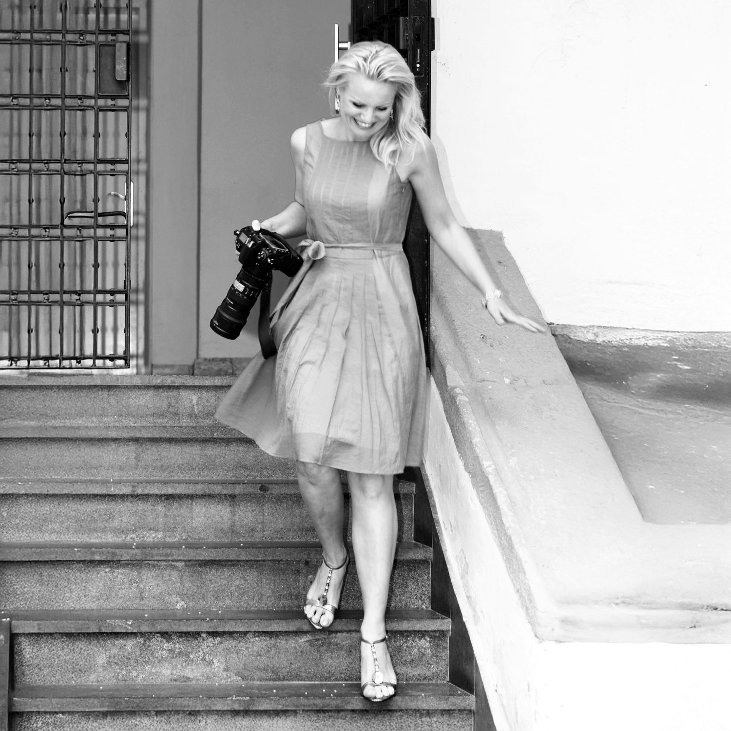 Vintage black and white photo of woman in light dress descending outdoor steps while holding a camera.