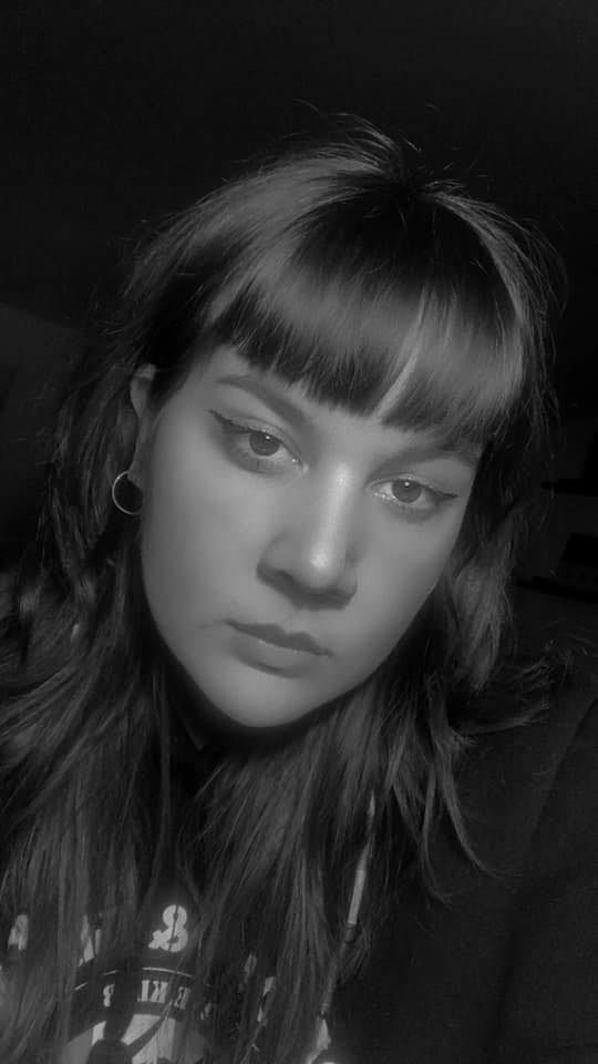 A black and white portrait photograph showing someone with dark bangs and minimal makeup in a moody lighting setup.