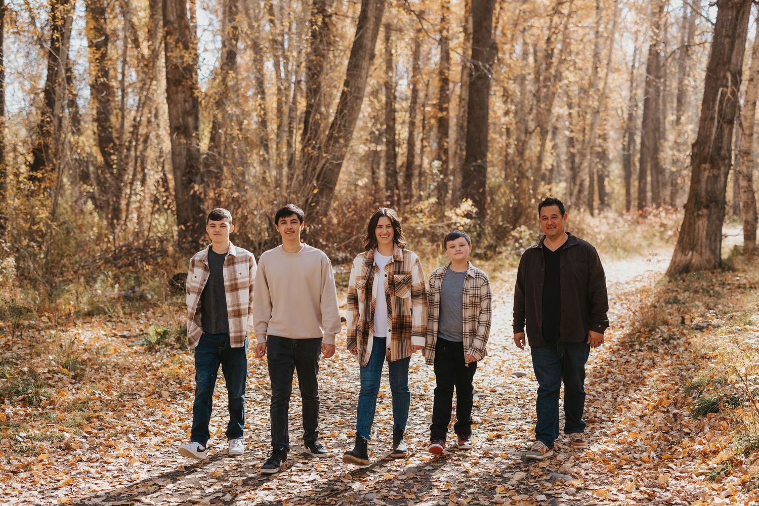 A group of people standing together on a forest path during autumn with fallen leaves and bare trees.