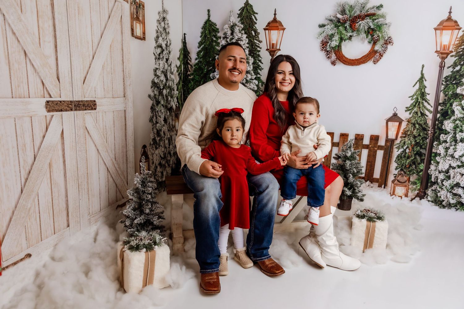 A group poses for Christmas holiday photos in a festive white barn setting with evergreen trees and winter decor.
