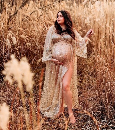 Dreamy maternity photo in wheat field with woman wearing shimmering gold dress at sunset.