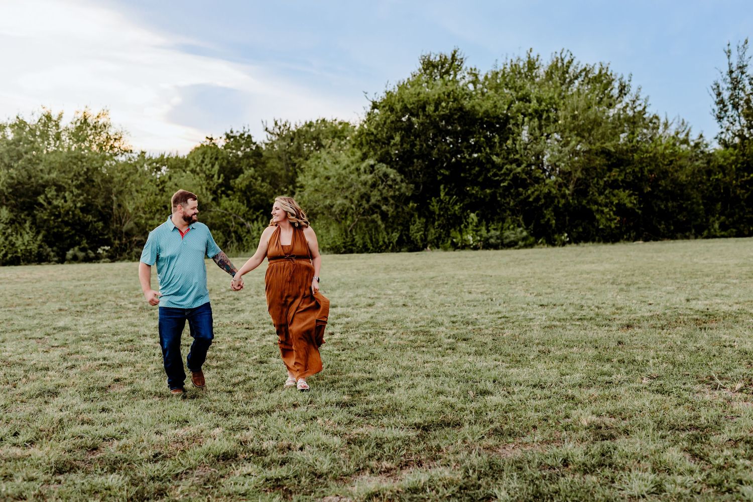 Two people walk together on a grassy hillside on a sunny afternoon.