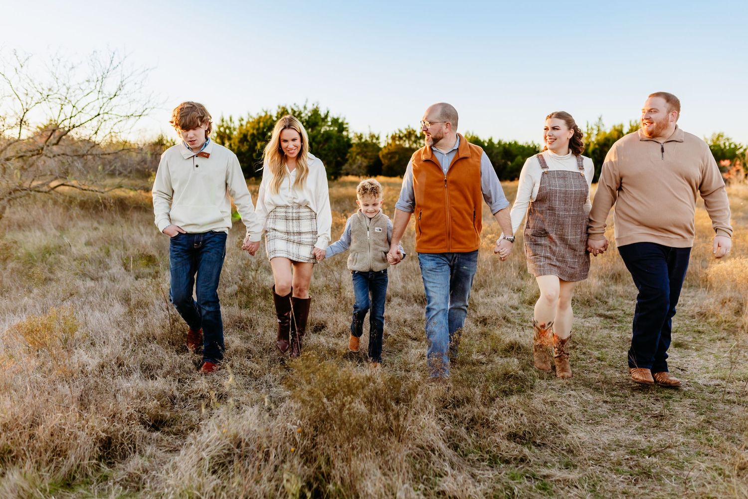 Family walking together through a grassy field at sunset while wearing casual fall attire.