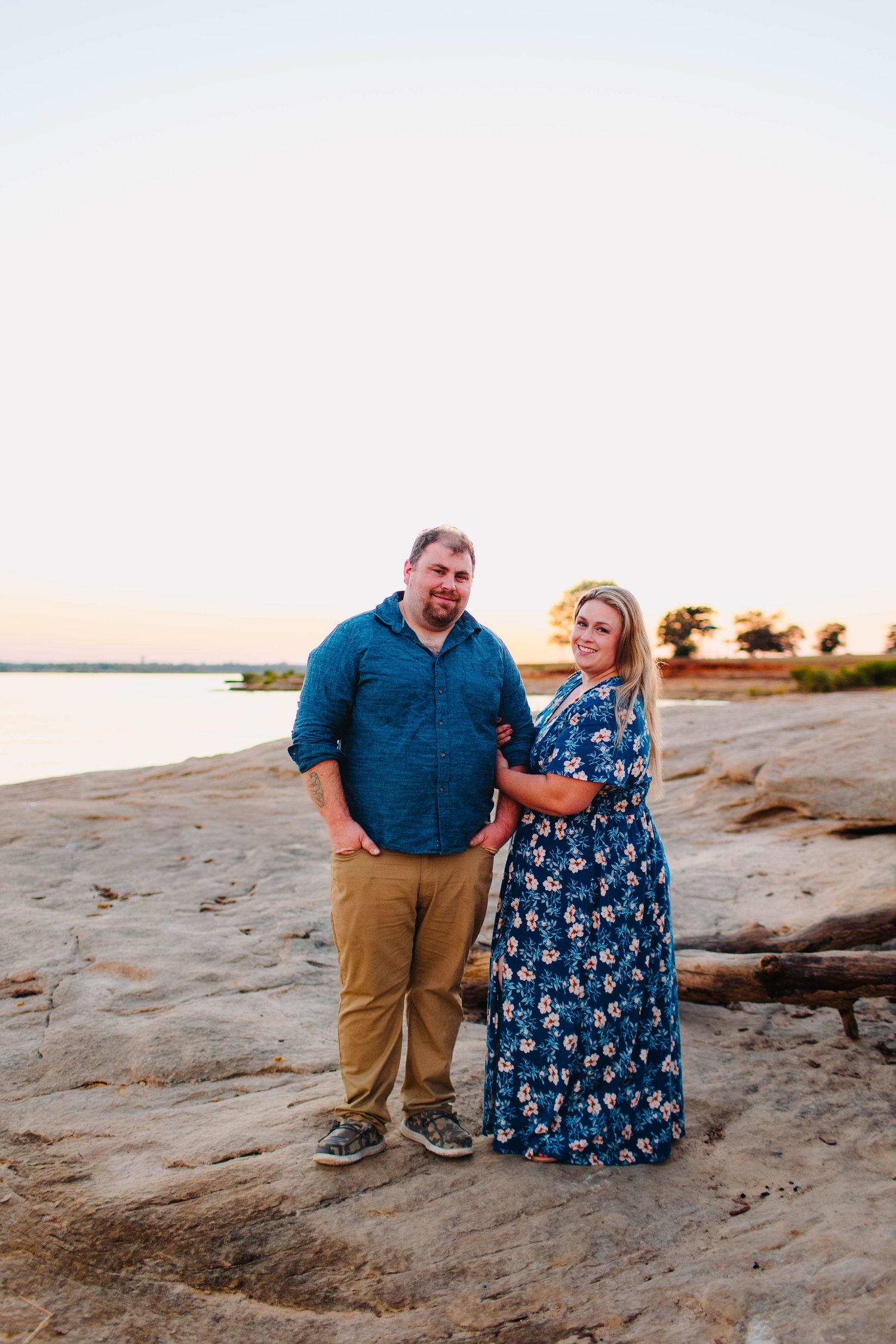 Romantic couple portrait on a rocky beach at sunset wearing coordinated blue and floral outfits.