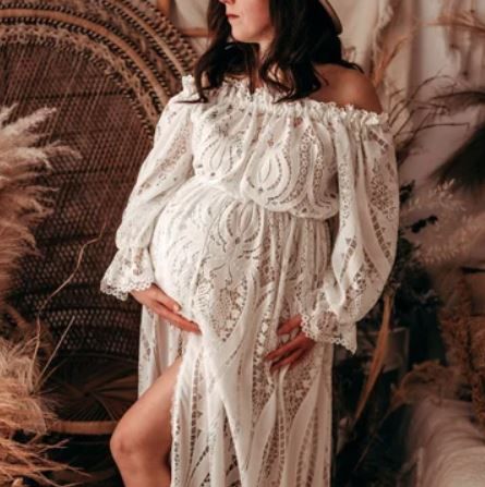Romantic maternity photo with lace off-shoulder dress against peacock chair and dried flowers.