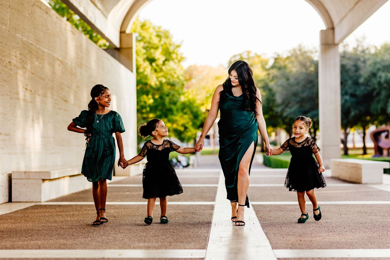 Mother and daughters in matching green dresses walking under stone archway.