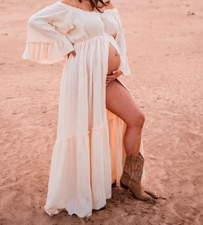 Desert maternity photo featuring white flowy dress and cowboy boots on sandy terrain.
