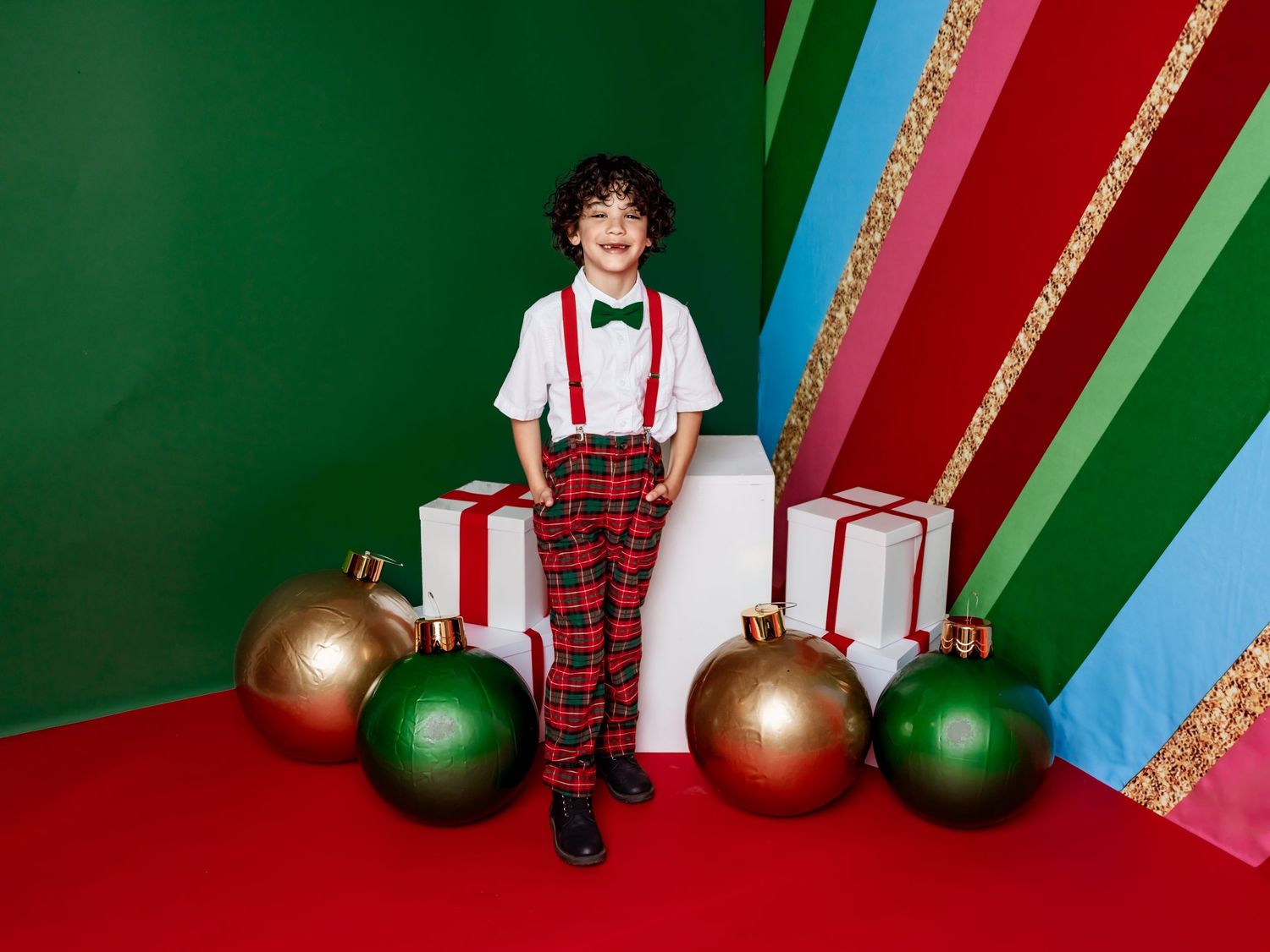 A person wearing festive red plaid sits amongst holiday decorations against a red and green studio backdrop.