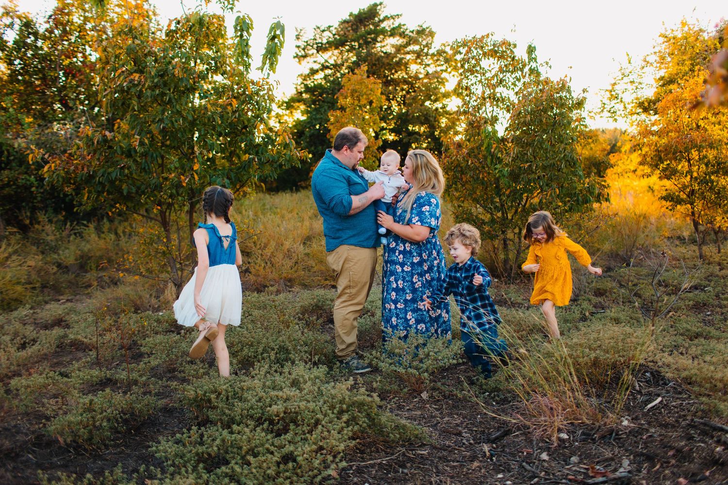 A group in coordinated blue and yellow outfits pose together in a sunlit autumn field during golden hour.