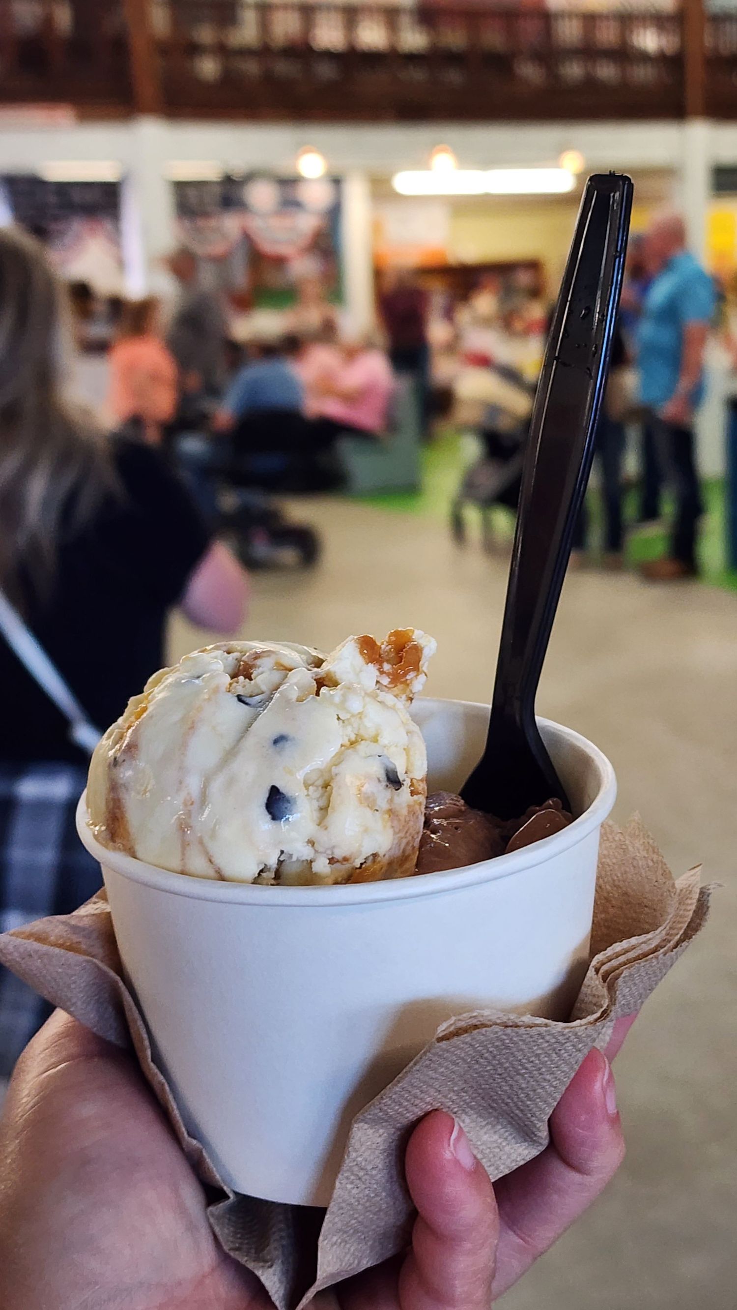 Hand holding a paper cup with two scoops of Tillamook Ice Cream and plastic spoon stock in it.
