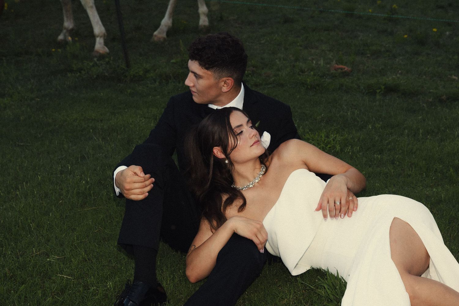 A couple in wedding attire shares an intimate moment while laying on grass during an outdoor photo session.