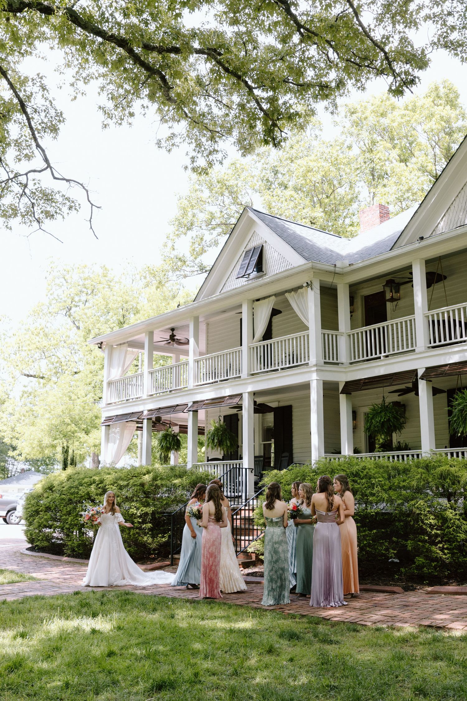 Bride and bridesmaids in colorful gowns gather outside a white Southern colonial mansion with wrap-around porches.