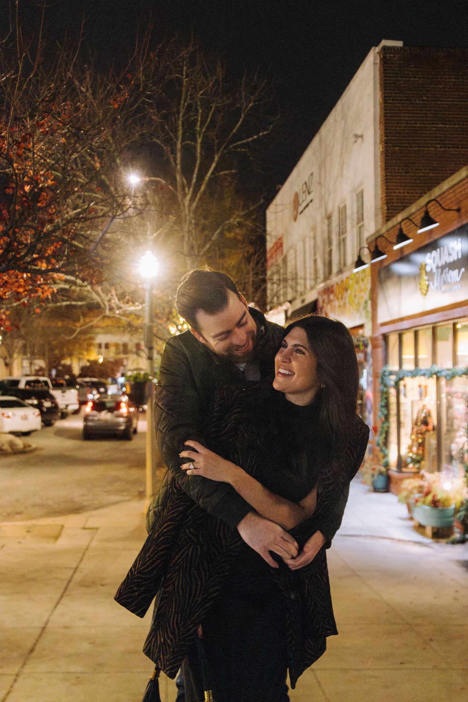 A couple shares joyful laughter while embracing on a quiet, lamp-lit street at night during autumn.